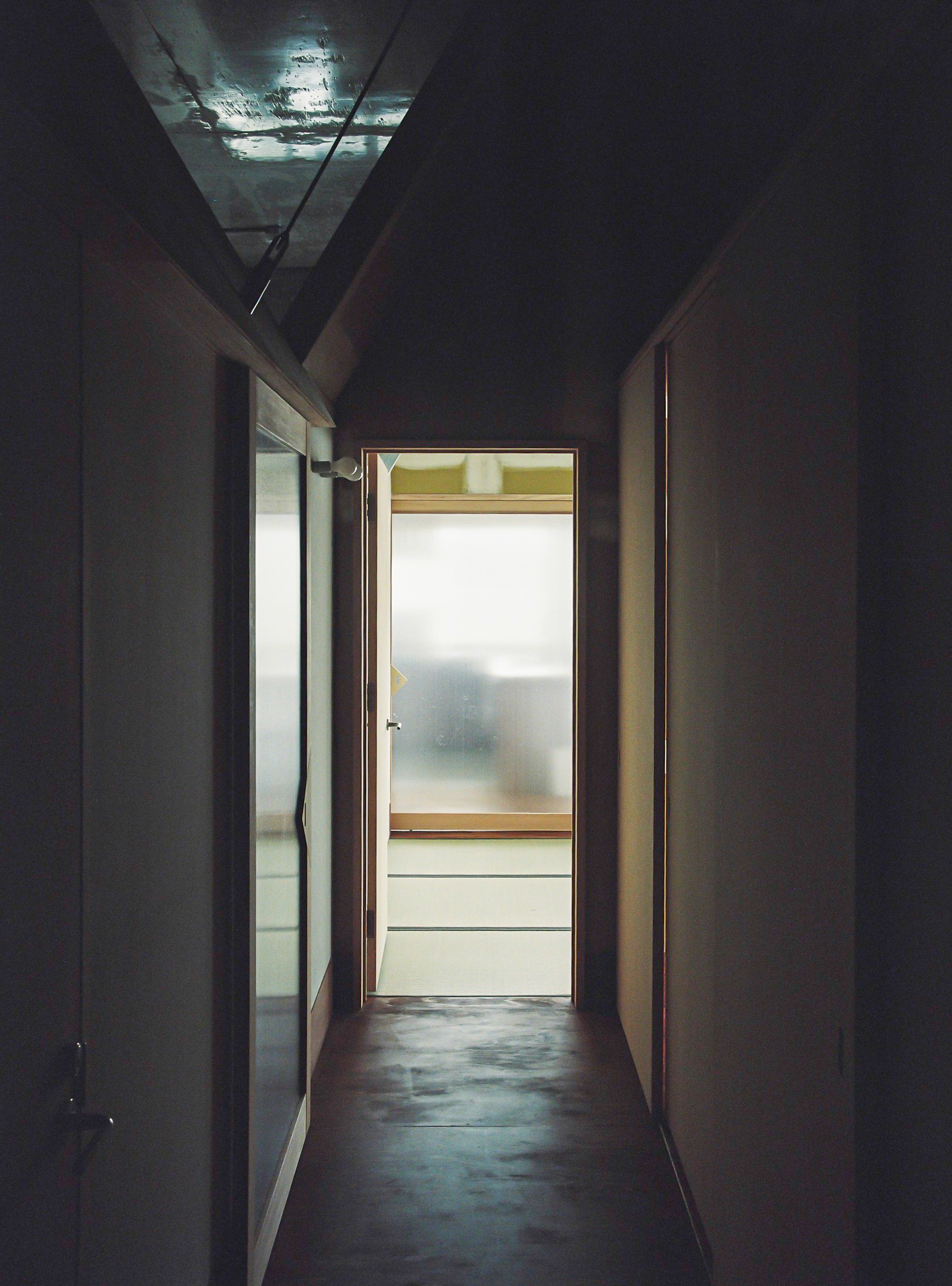 Corridor view at dusk with backlit door frame and reflective concrete ceiling catching exterior light