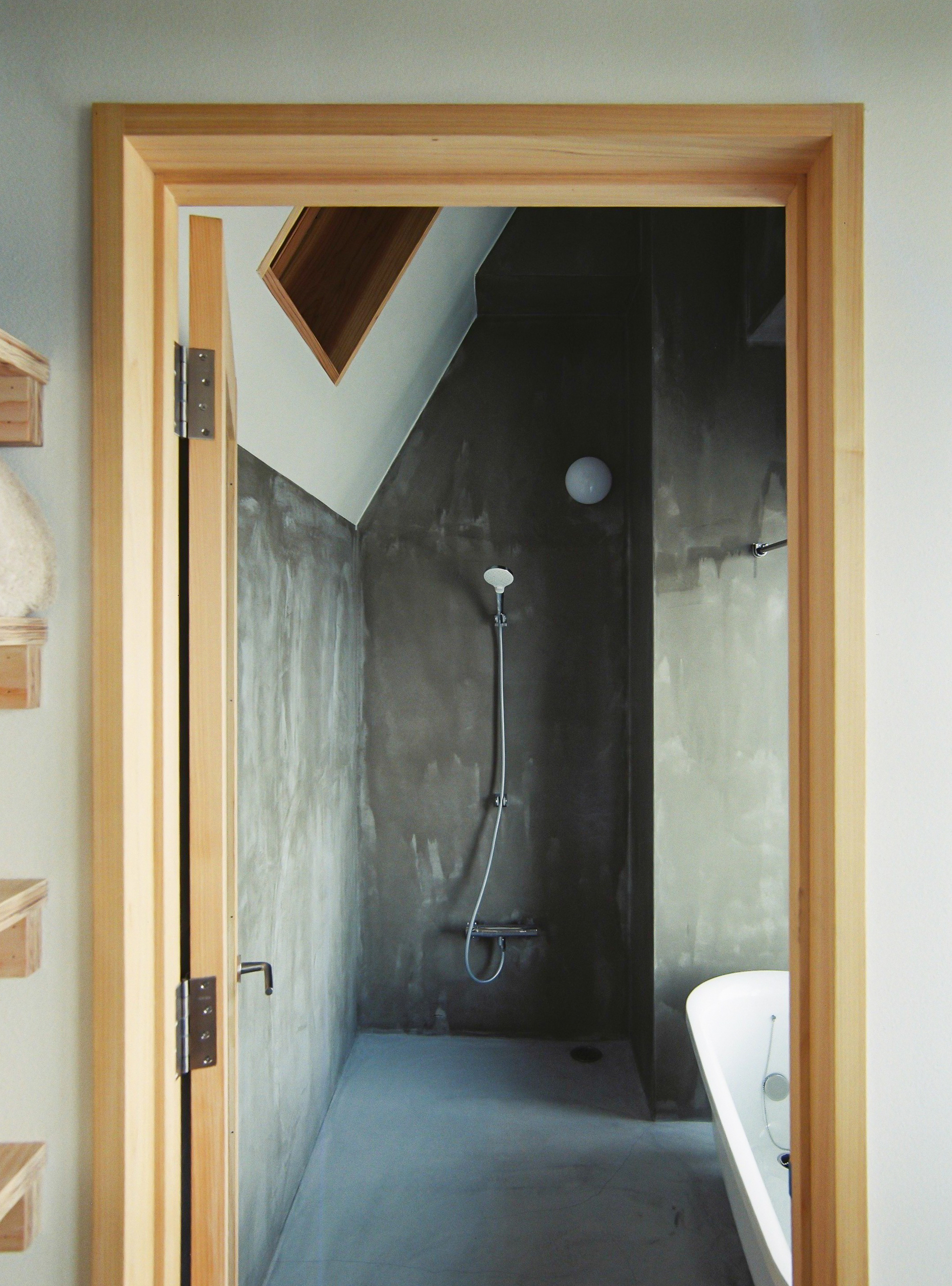Bathroom with polished concrete walls, timber-framed doorway, wall-mounted shower and angled skylight overhead