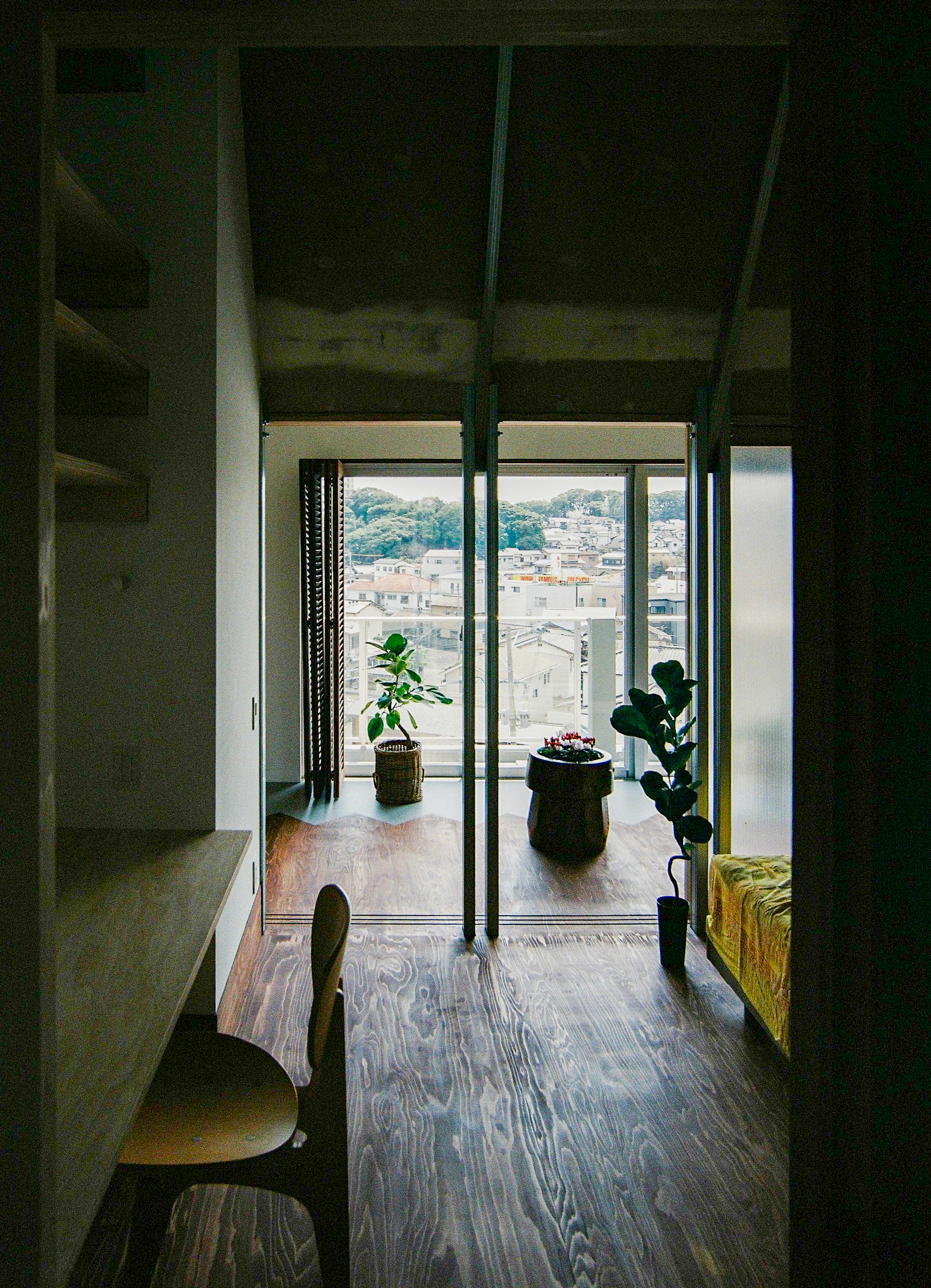 Interior corridor looking toward balcony with potted plants and hillside rooftops visible through glazed doors