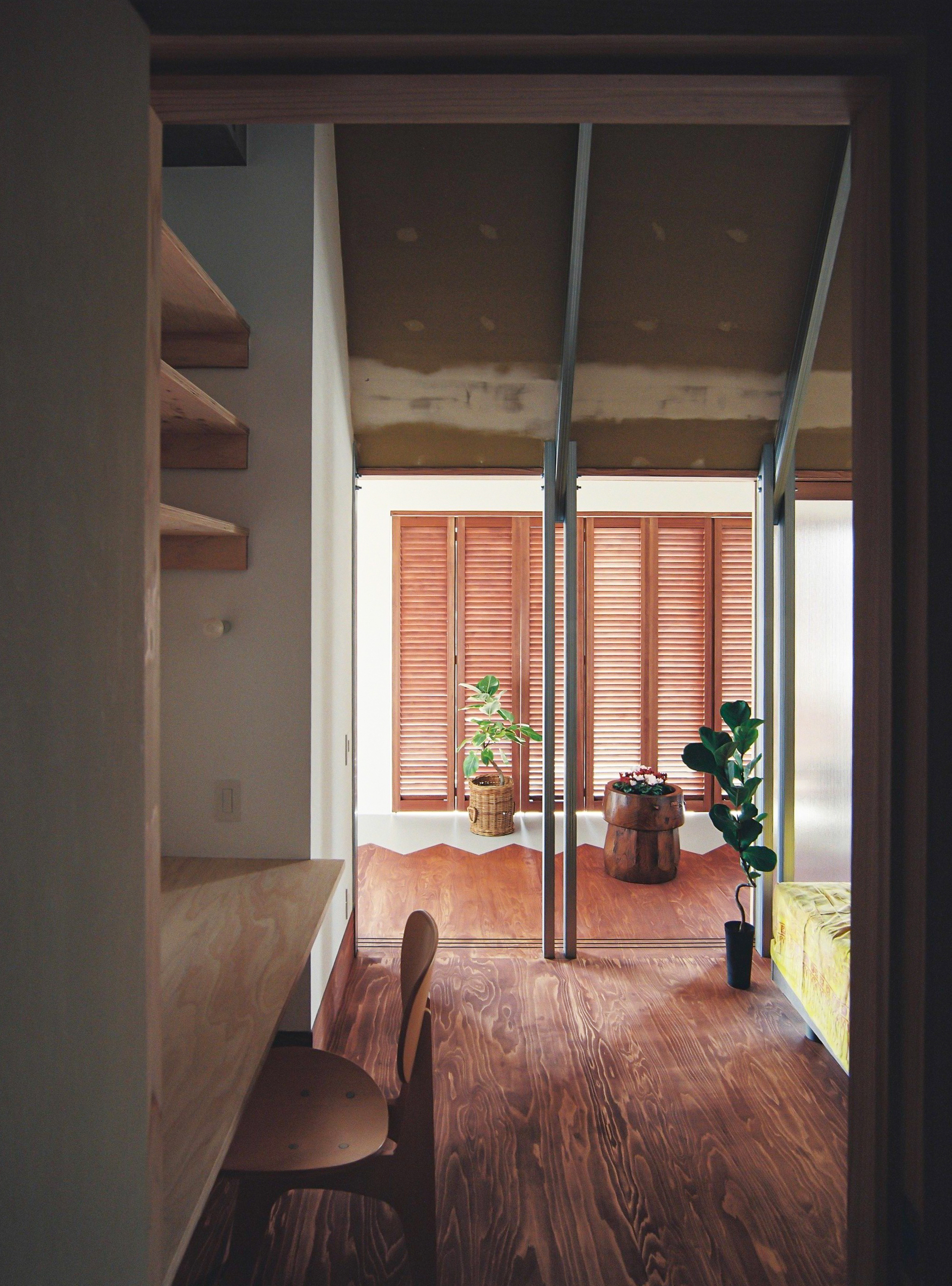 View through room toward balcony with timber louvered shutters, potted plants and timber flooring in afternoon light