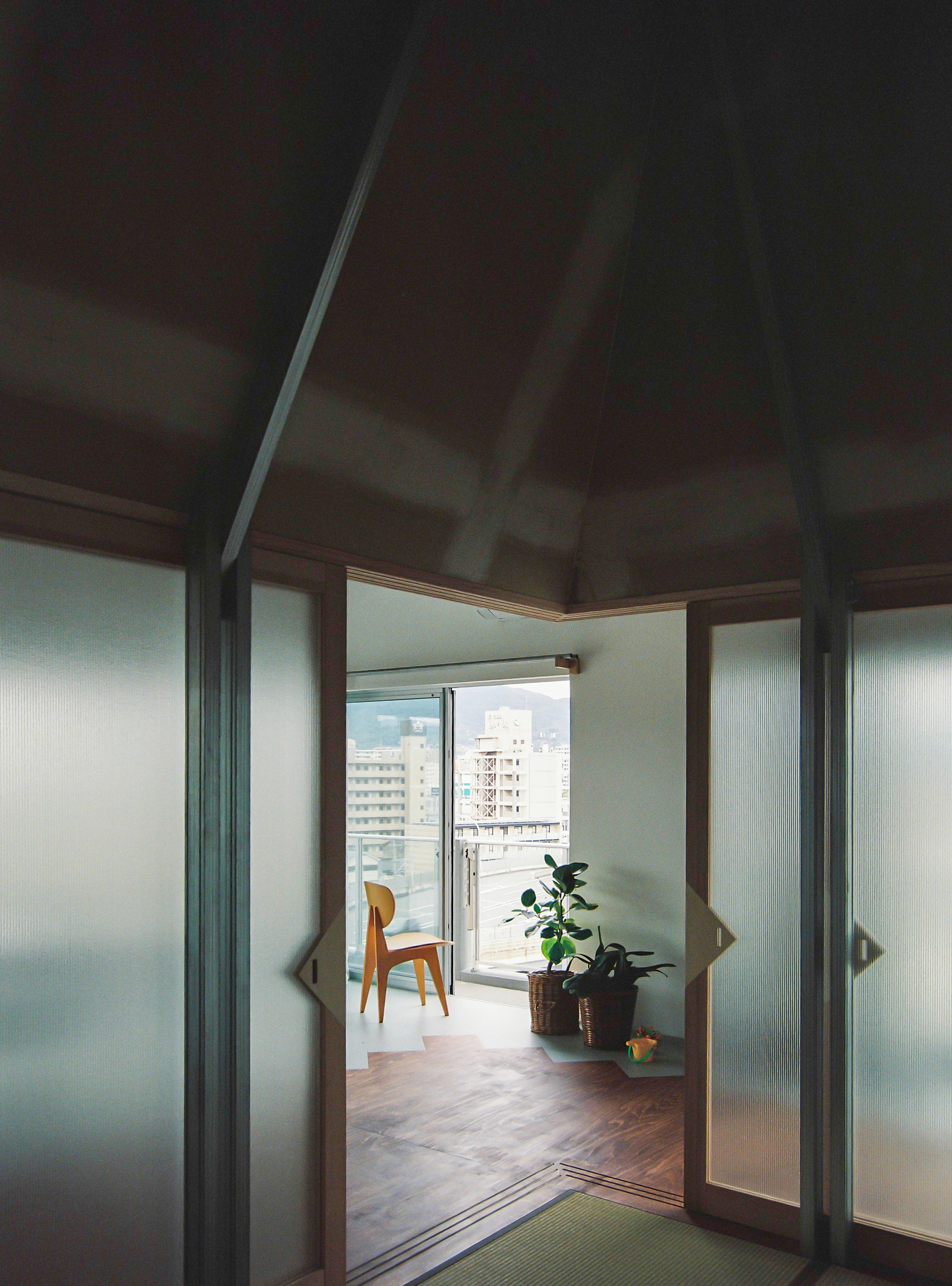 View through translucent sliding panels into a room with a balcony and chair overlooking apartment buildings