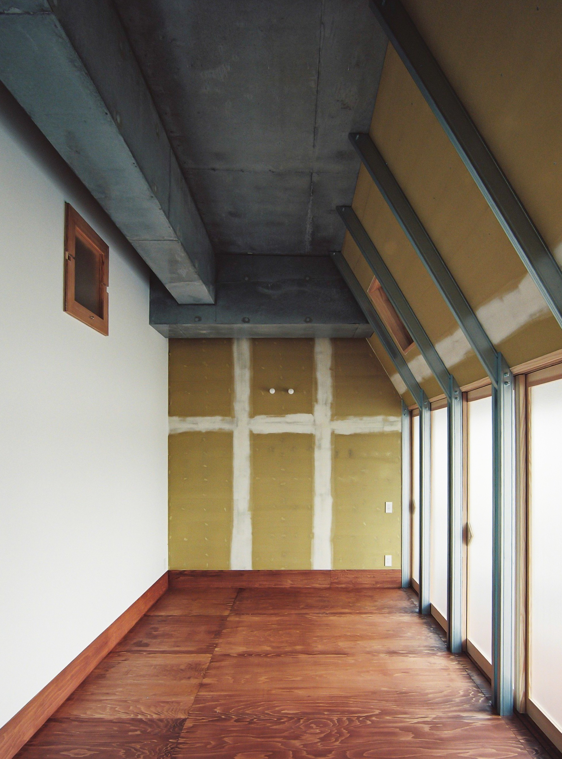 Interior room with exposed concrete ceiling beams and mustard wall showing structural tie marks beside glazed doors