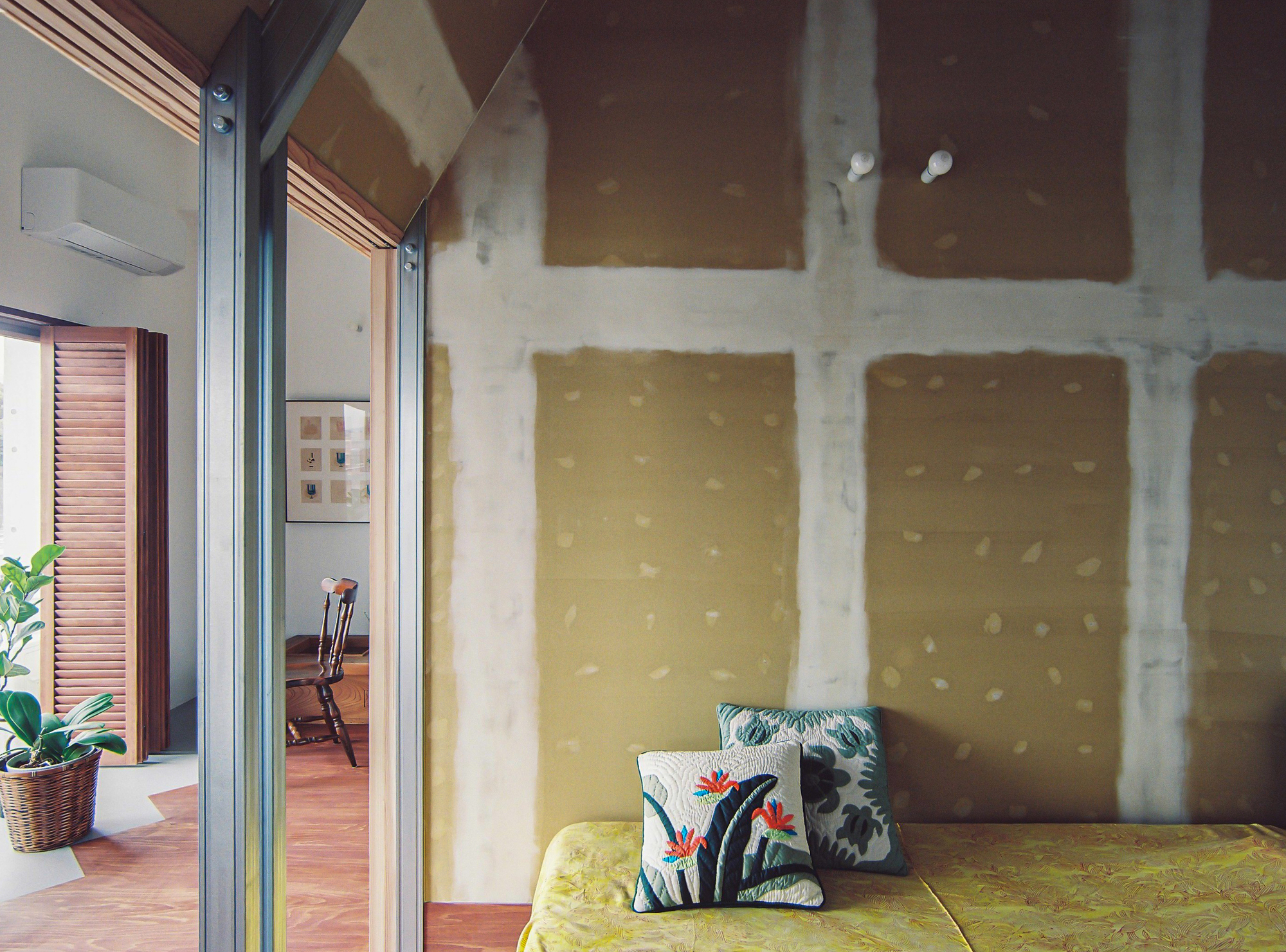 Corner nook with upholstered daybed against a mustard wall showing visible tie holes from concrete formwork