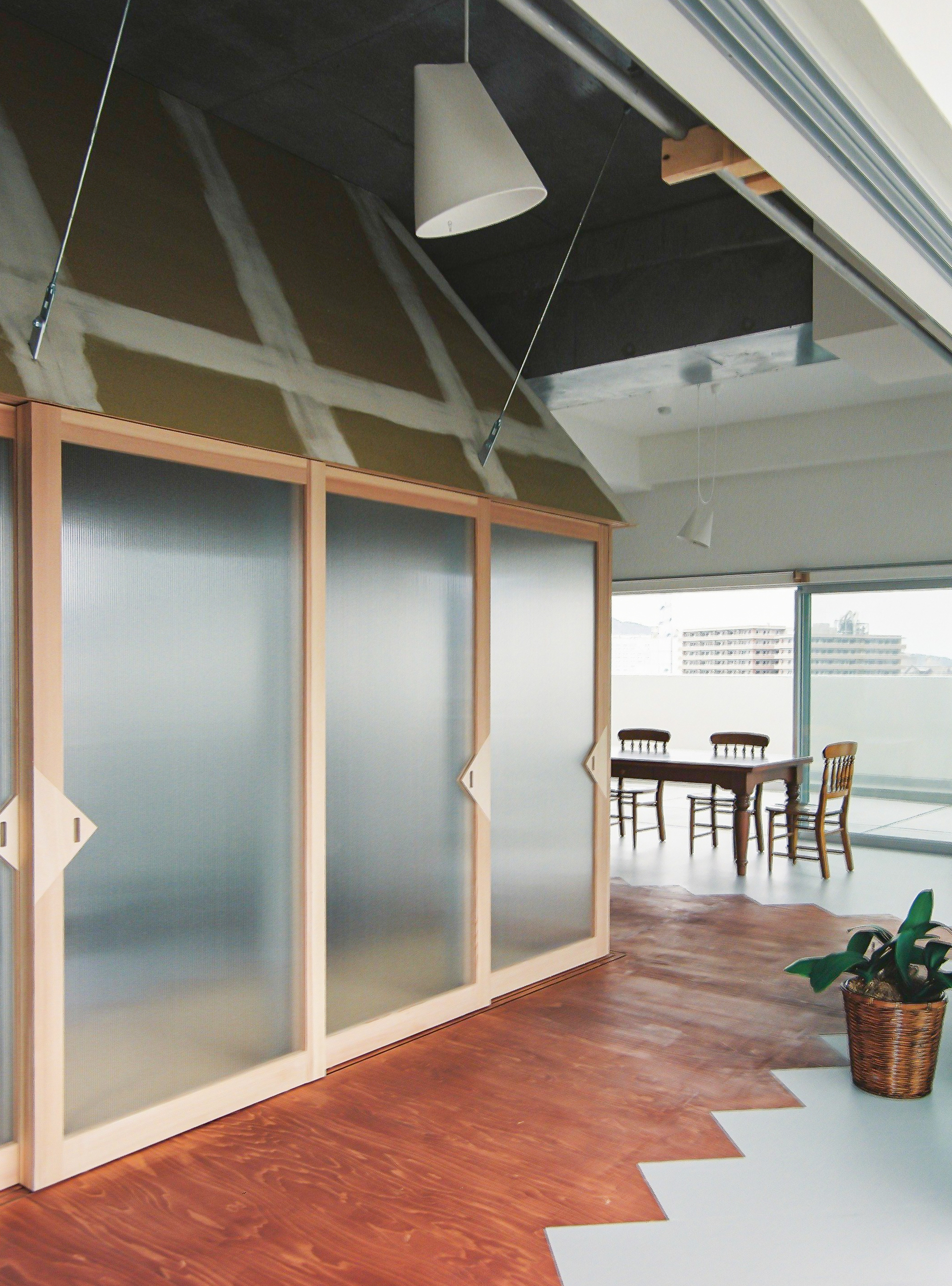 Interior space with frosted glass partition in timber frames and zigzag wood flooring pattern meeting pale linoleum