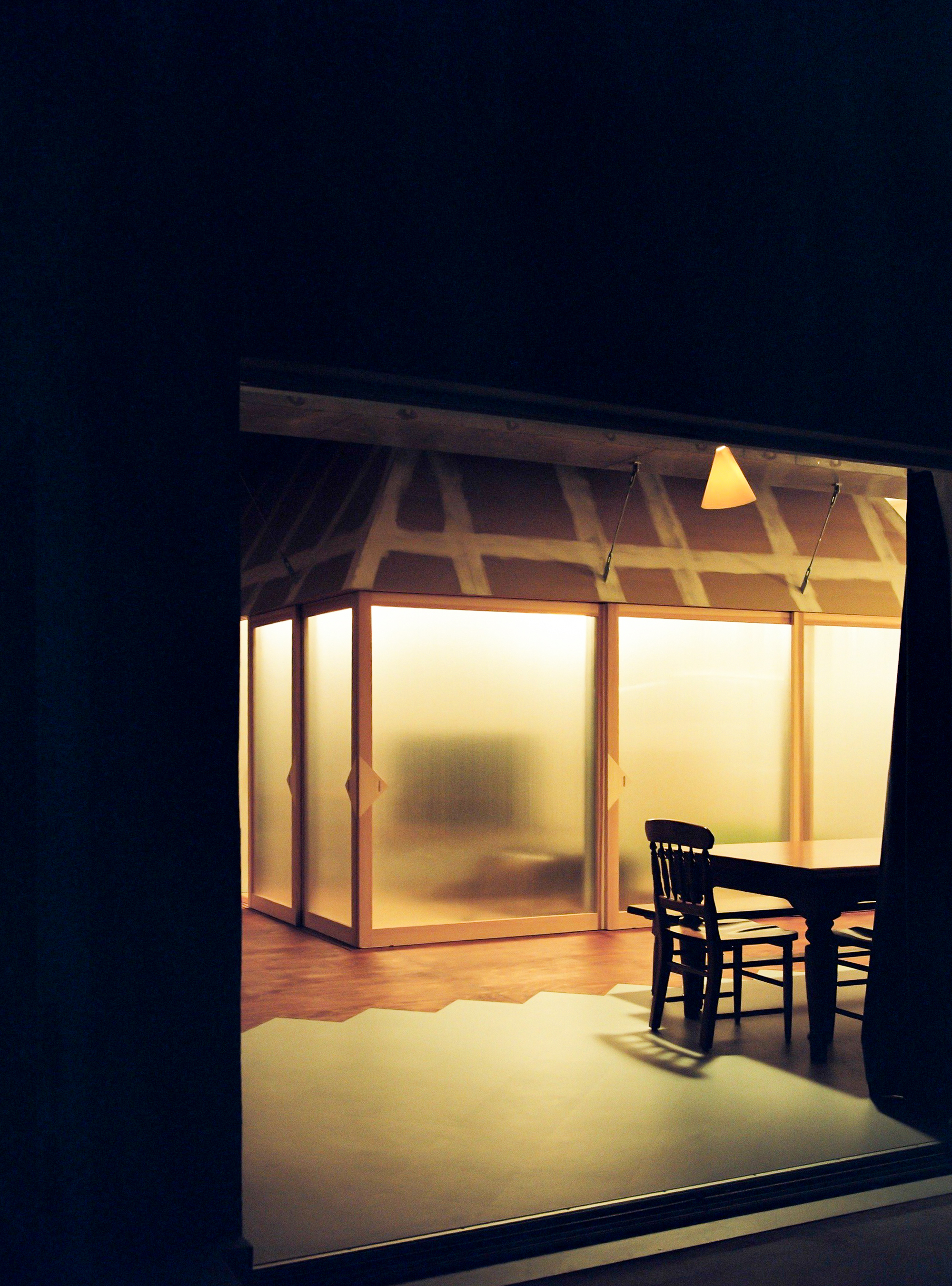 Interior room with frosted sliding screens and exposed timber roof structure glowing at night