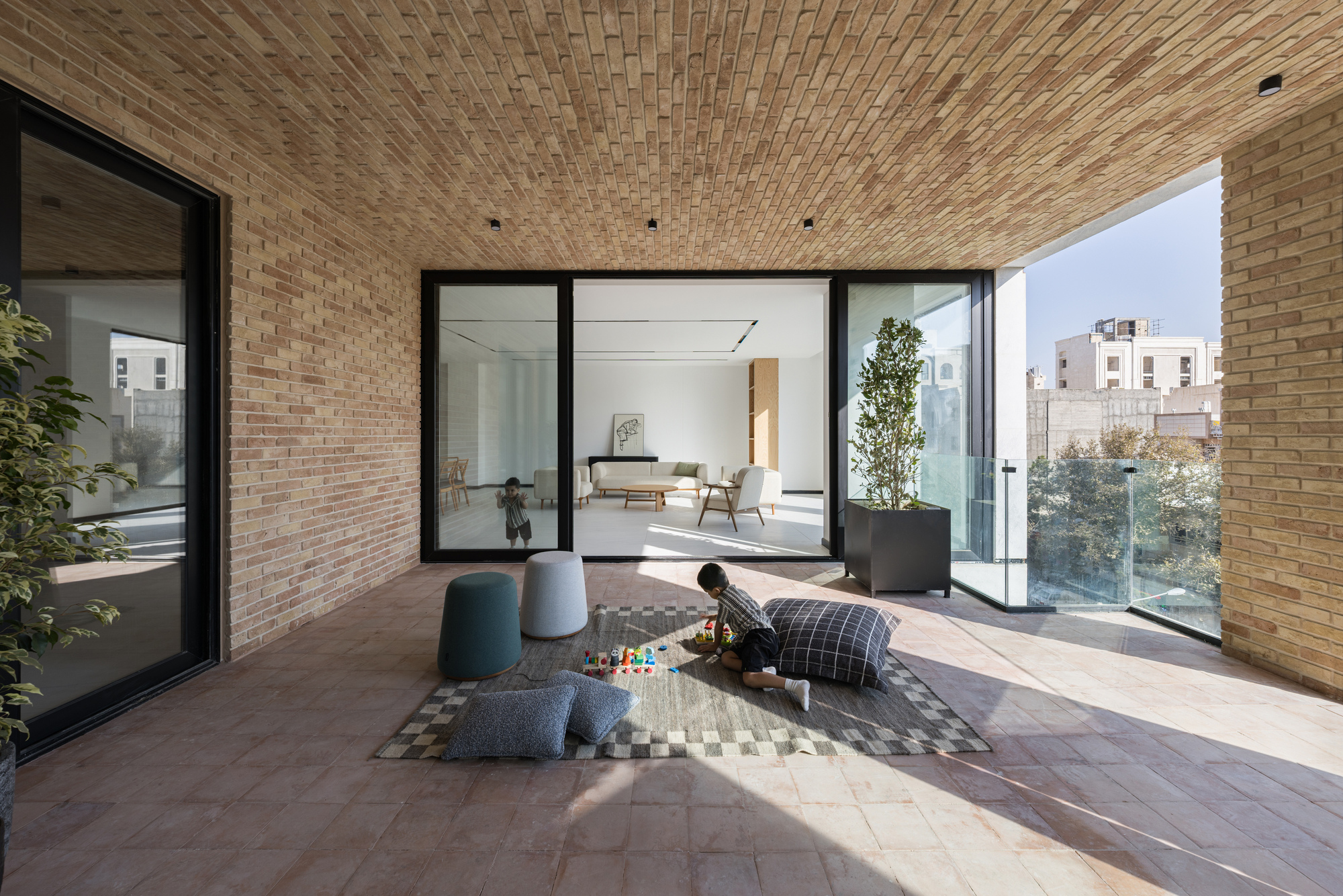 Private terrace with woven brick ceiling and planted trees framing views into the living room