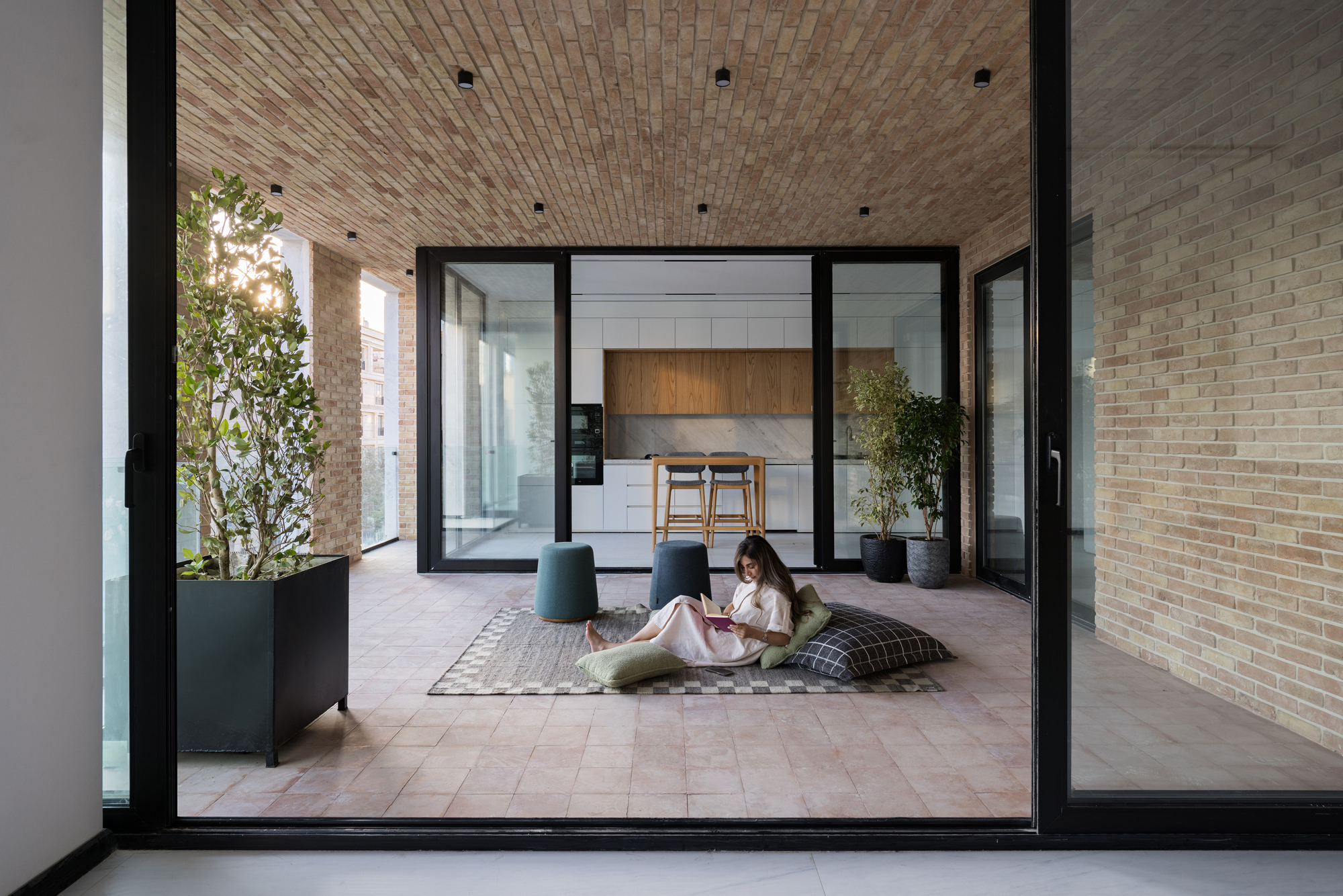 Outdoor terrace enclosed by glass walls with a person seated on floor cushions