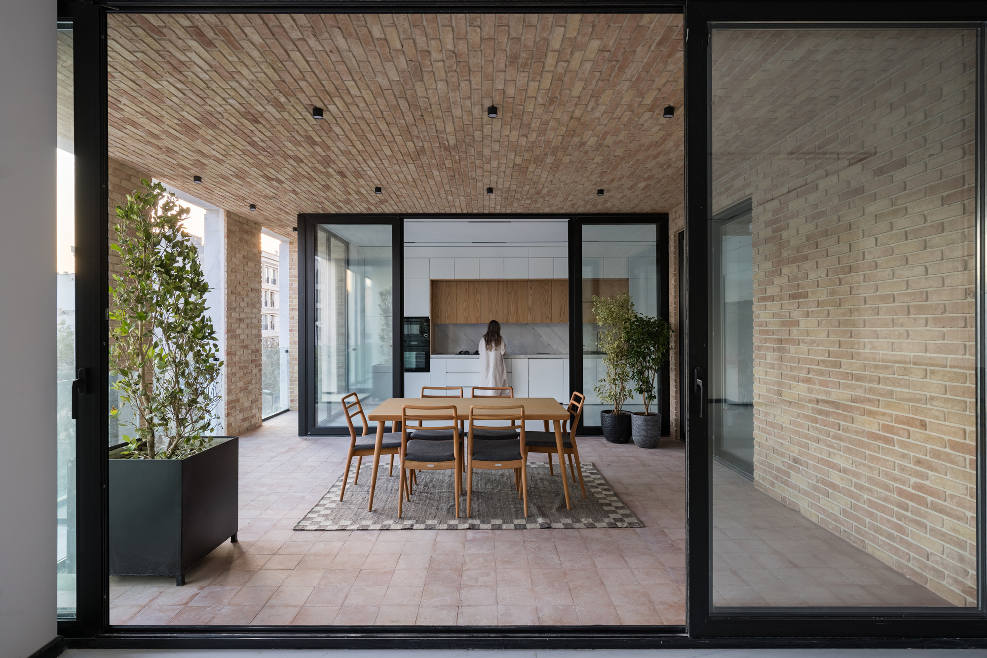 Dining area on terrace with timber table and chairs centered under a woven brick ceiling