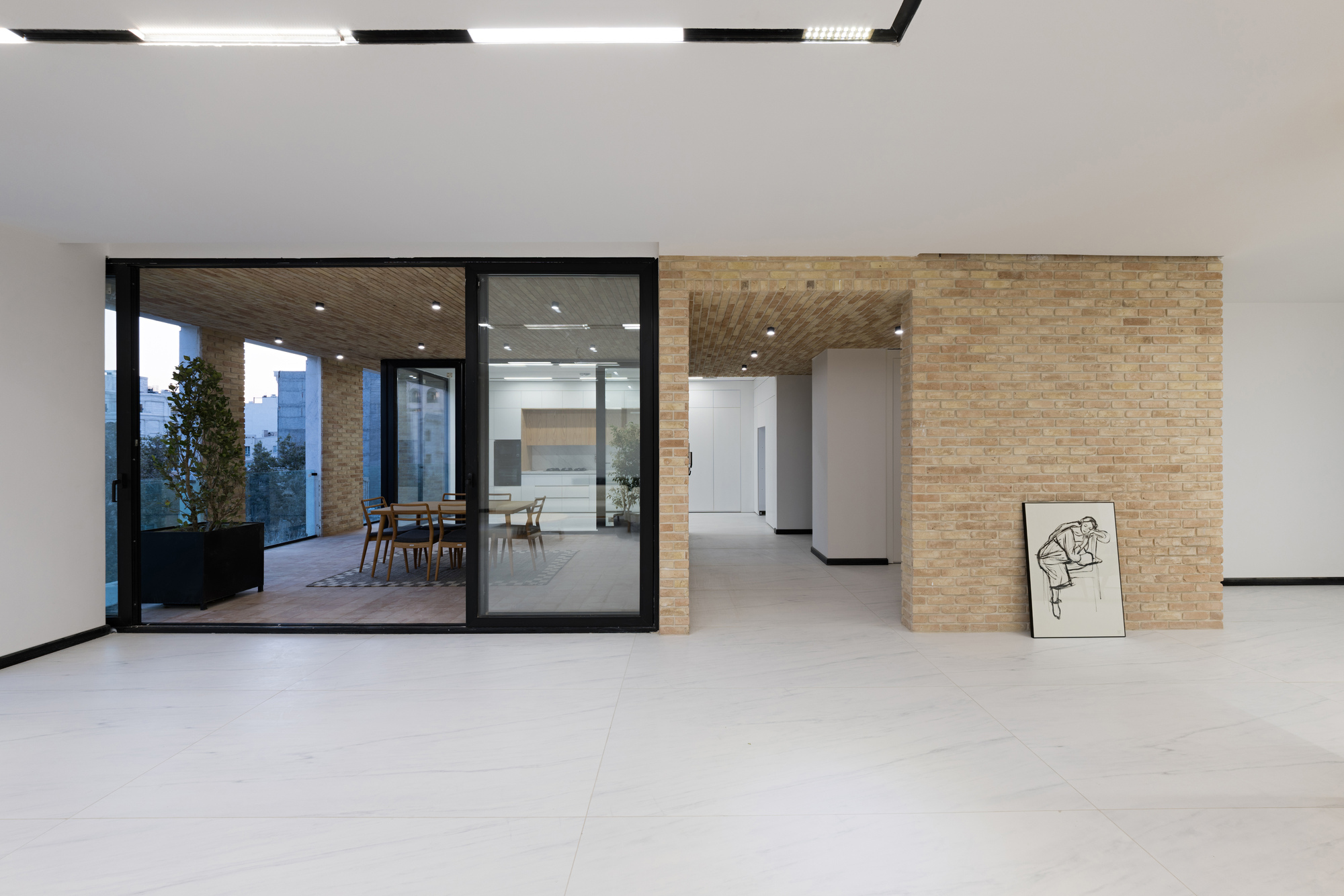Open plan interior showing textured brick volumes dividing spaces with pale stone floor and glazed terrace beyond