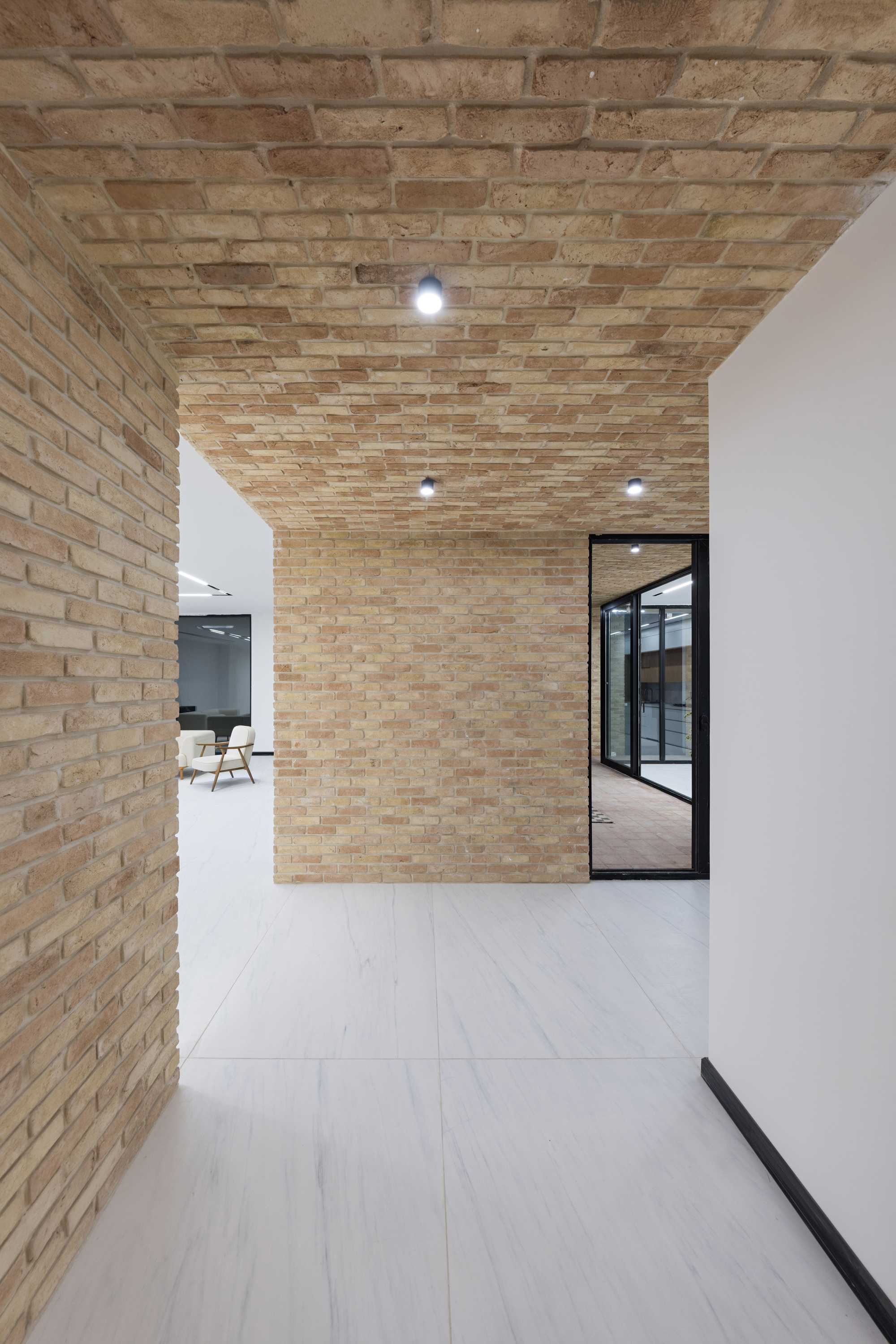 Corridor with textured brick wall and ceiling meeting white plaster surfaces under recessed lighting