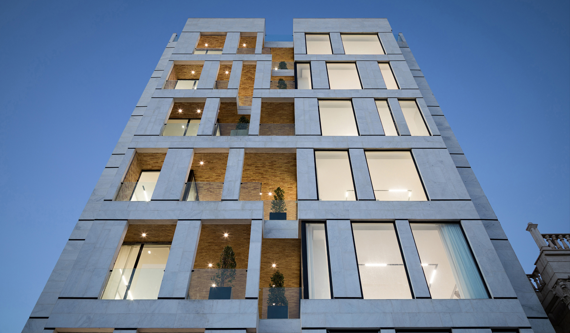 Frontal view of the illuminated facade at twilight with alternating concrete panels and recessed brick balconies