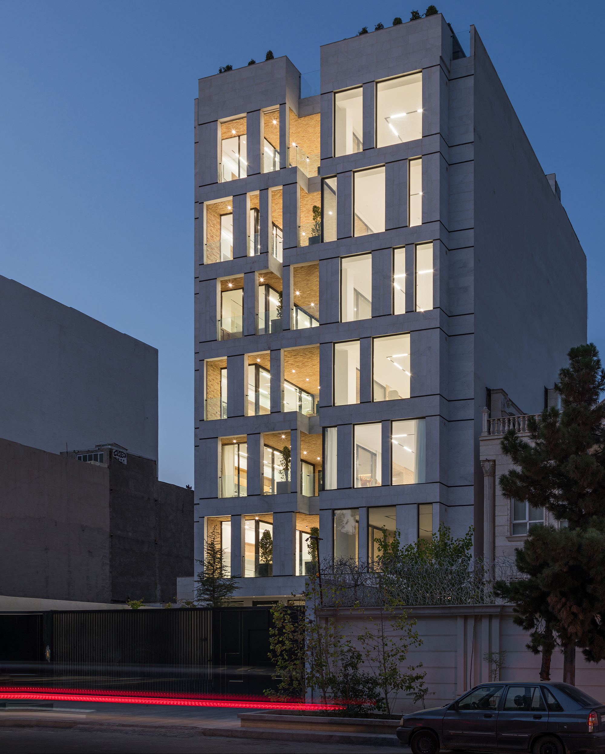 Street view of the illuminated concrete frame facade with recessed windows at dusk