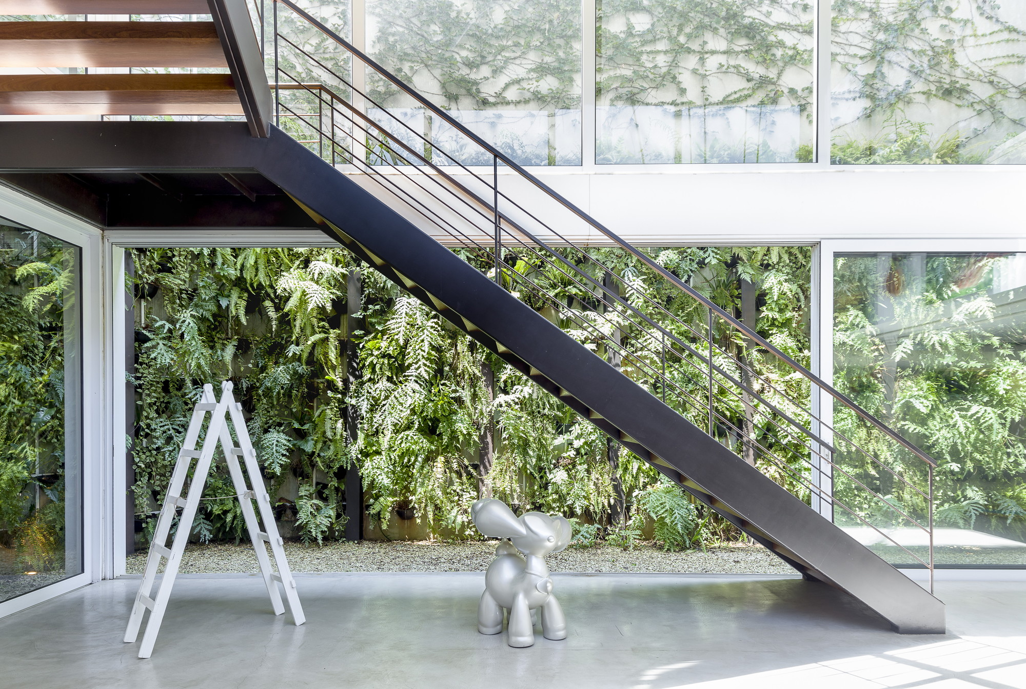 Black steel staircase with slim railing above a polished concrete floor, set against a fern wall with a small silver elephant sculpture