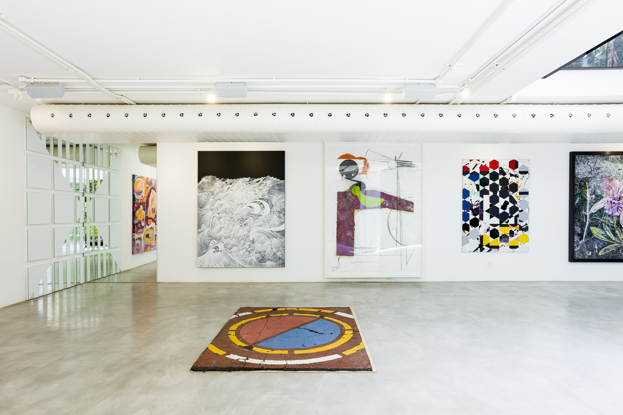Gallery wall of large framed paintings above a worn floor rug, with a white ventilation duct running overhead