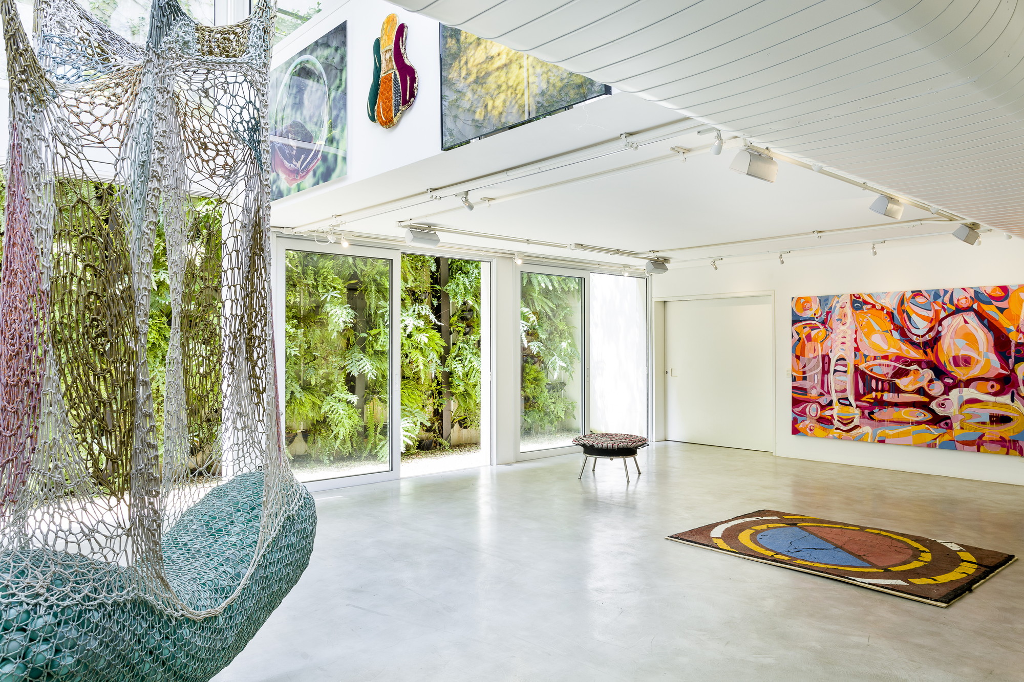 Gallery room with a hanging crocheted net seat, a colorful painted rug and a green living wall seen through sliding glass doors