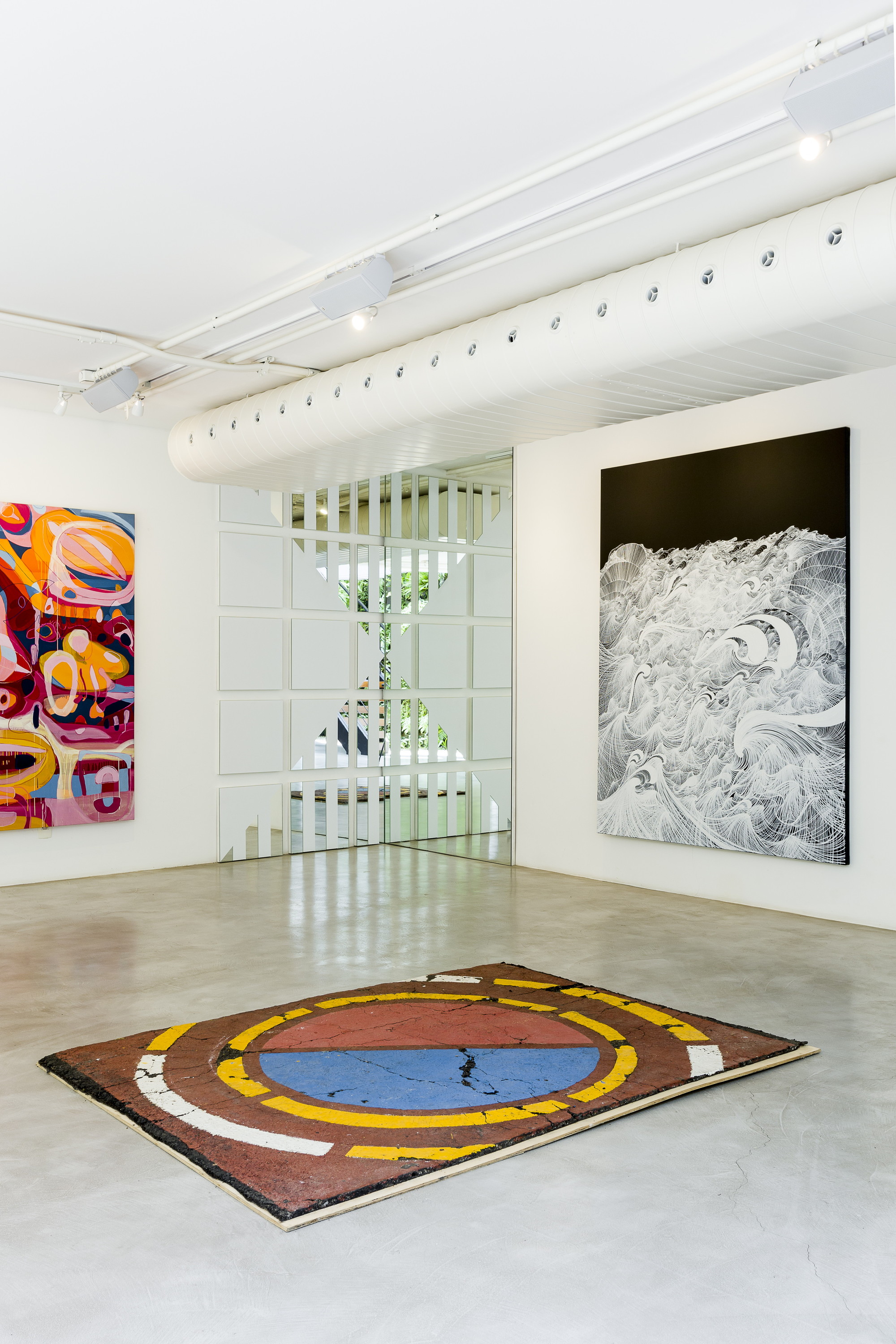 Corner of the gallery with a painted road-marking rug on the concrete floor, a wave drawing and a white perforated duct overhead