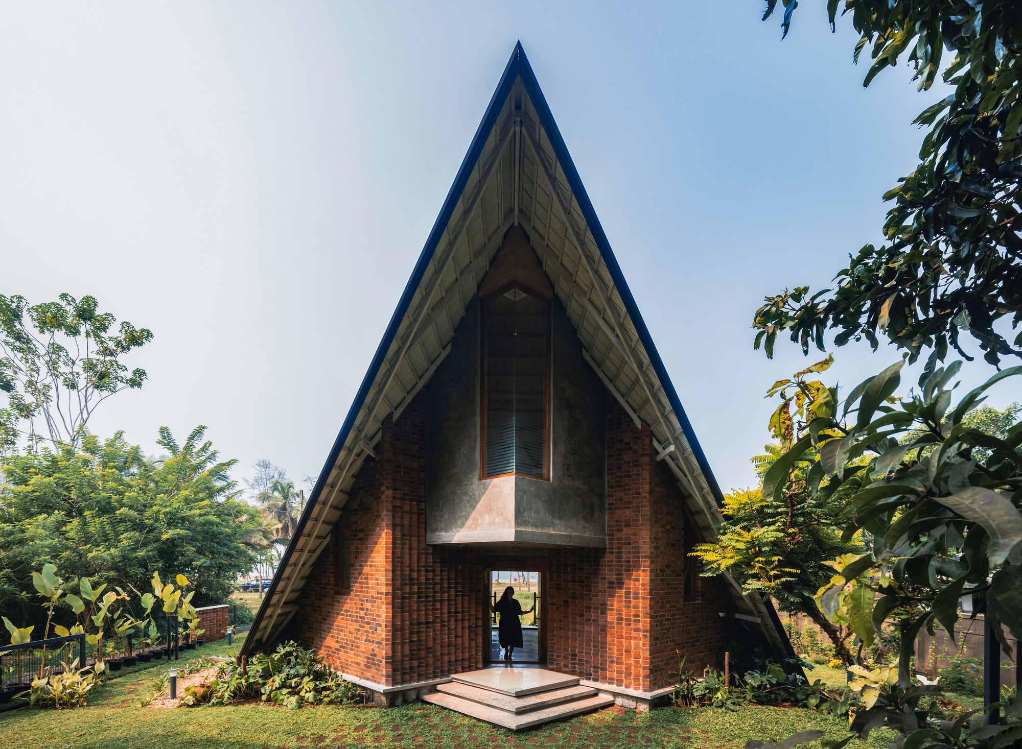 Frontal view of the triangular brick pavilion with steep roof and central entry door