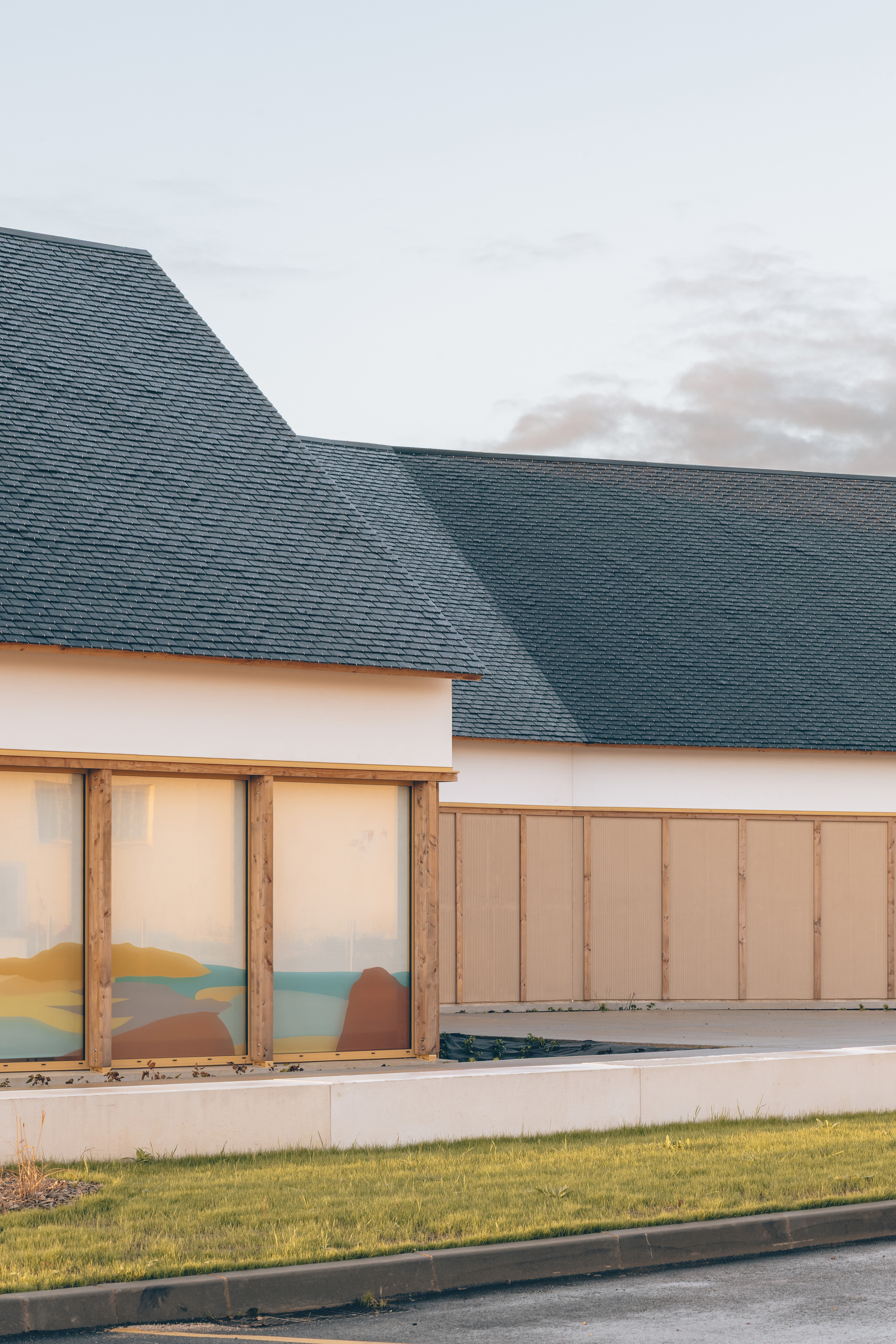Detail of the dark slate roof meeting white walls and timber-framed glazing with lawn in foreground