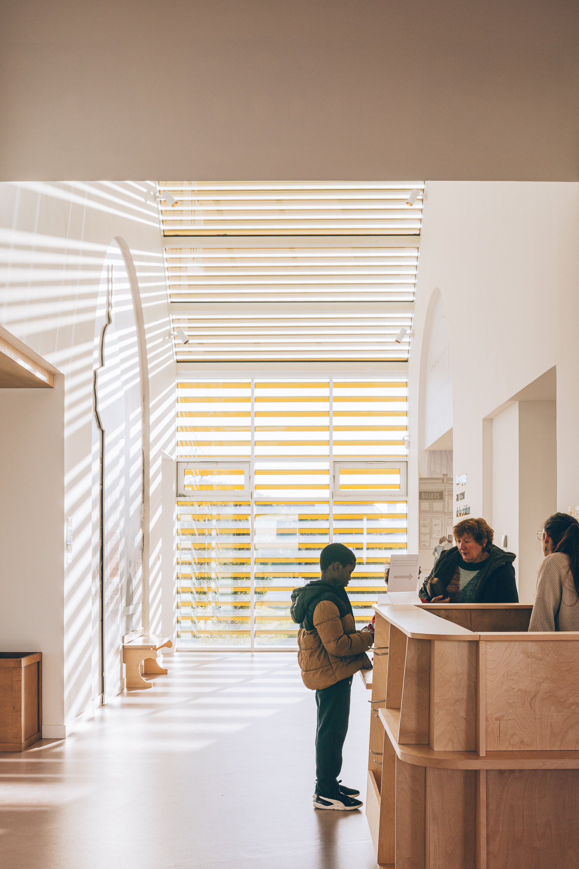 Reception desk with timber screen casting striped shadows across visitors in the entry hall