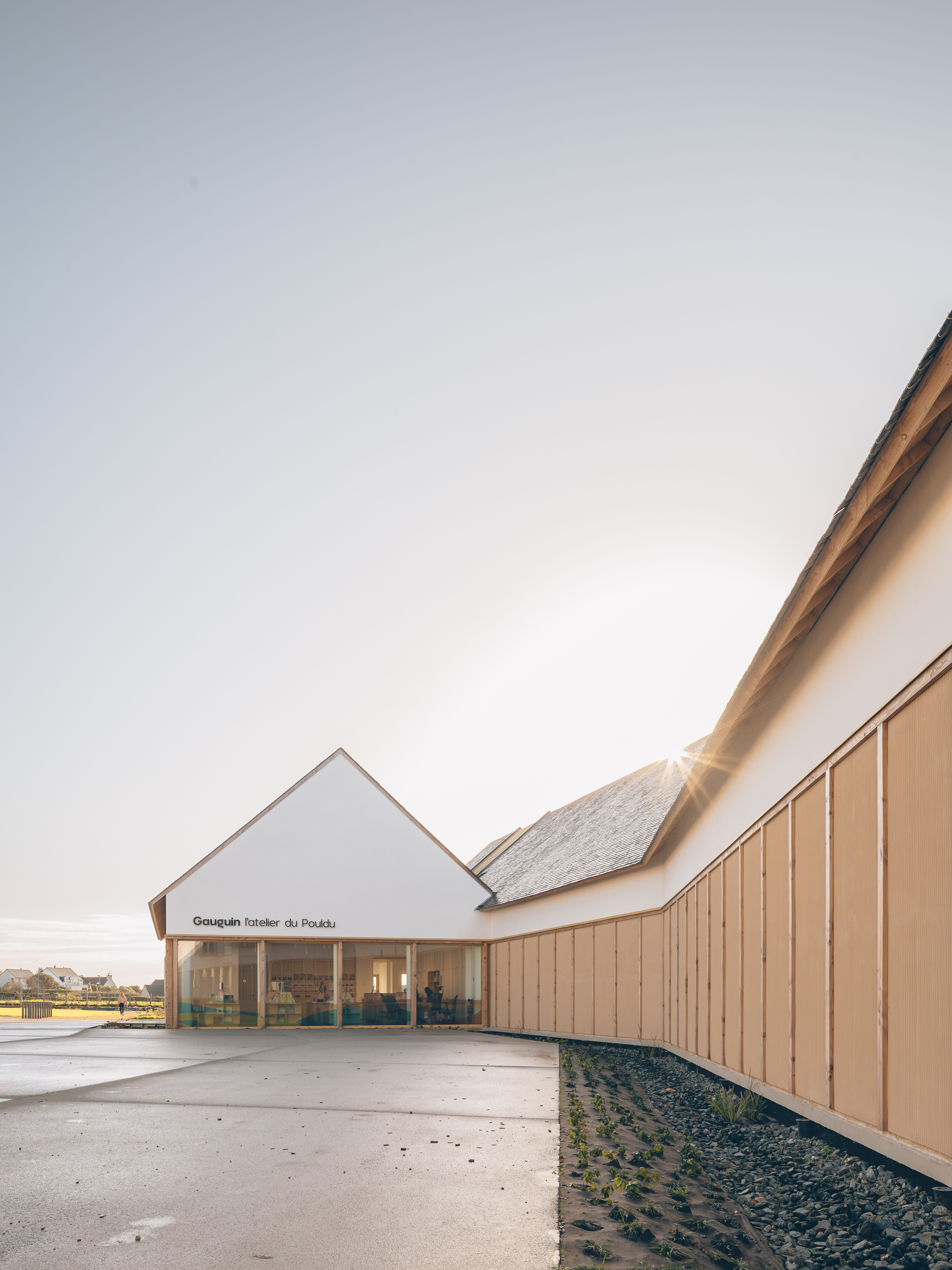 Angled view of the entrance gable and timber-clad wing with gravel base at sunset