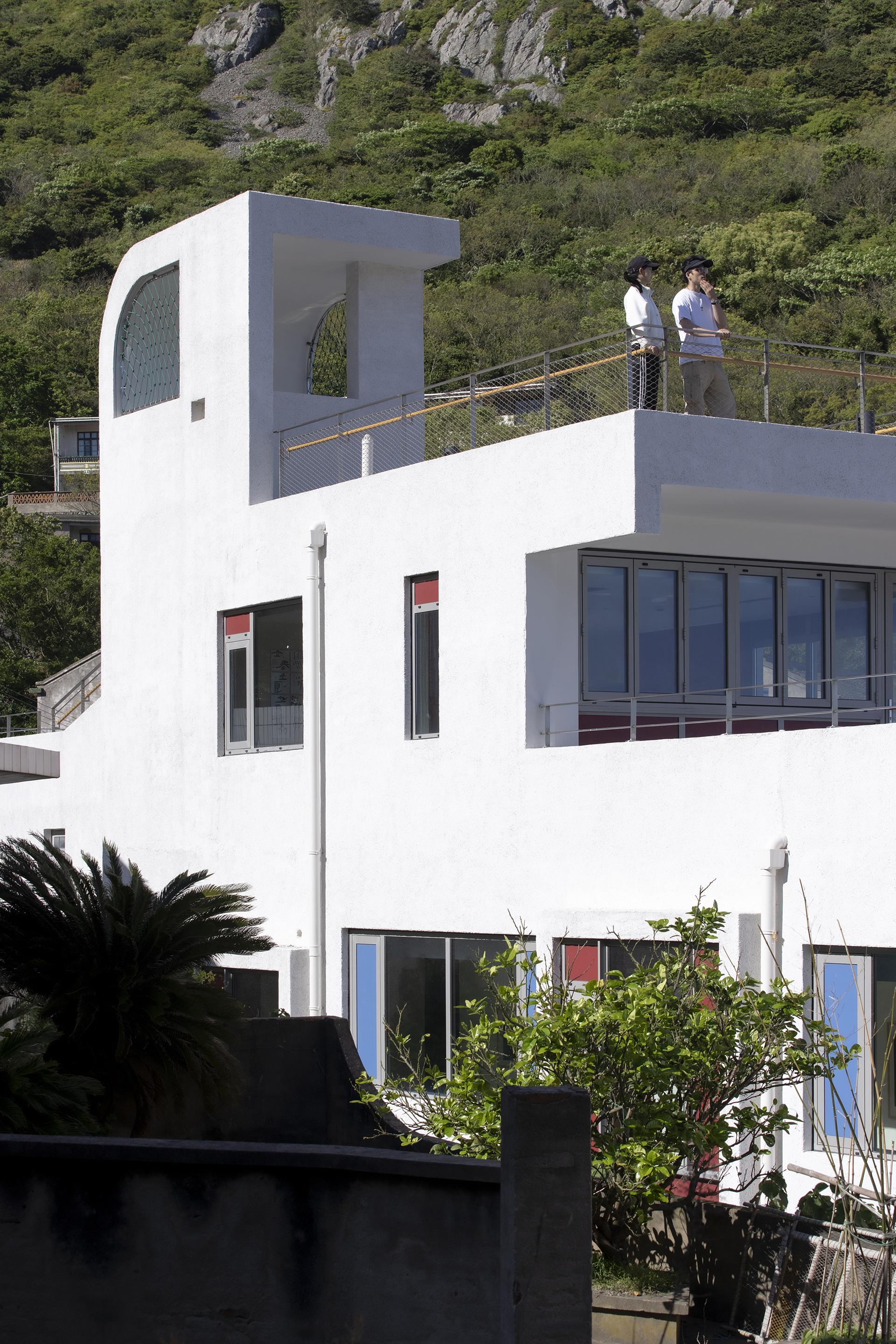 White rooftop terrace with curved tower element and two figures standing by the mesh railing