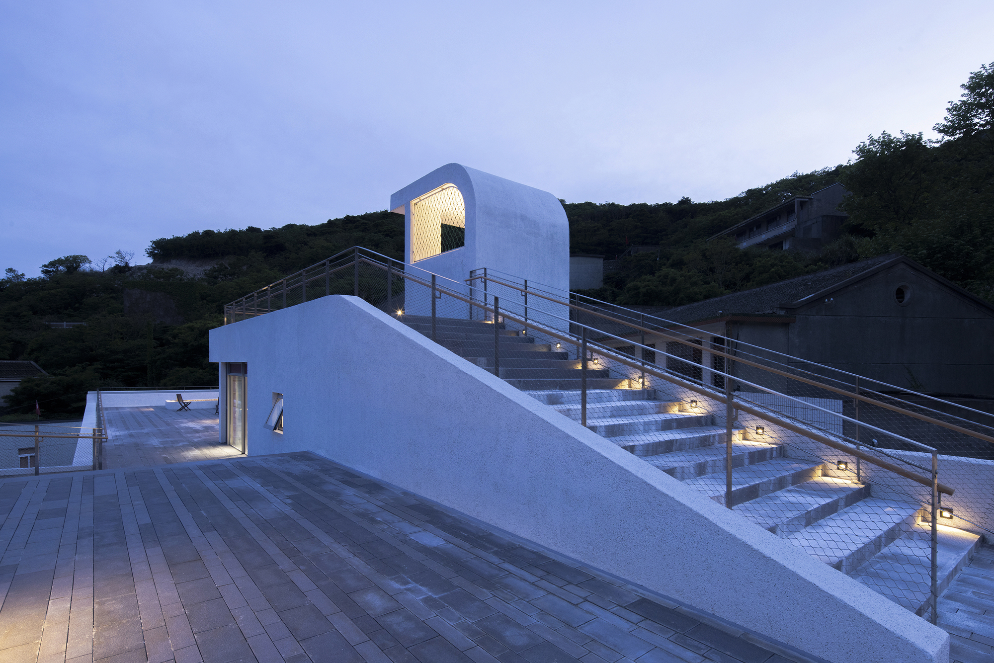 Illuminated staircase with metal railings ascending from a timber deck at dusk