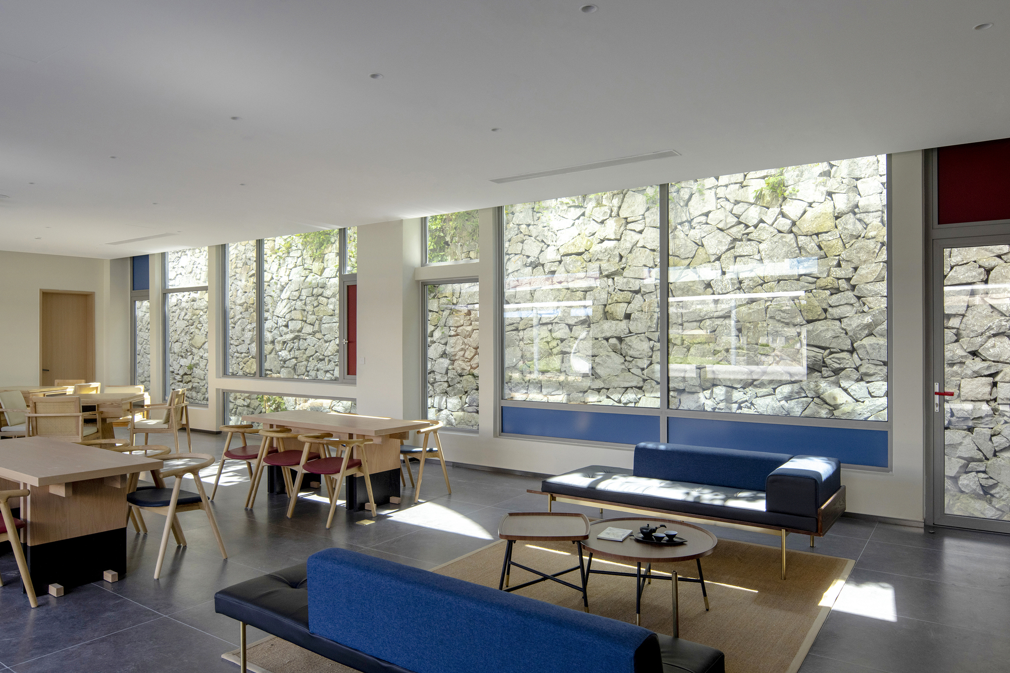 Interior space with floor-to-ceiling windows framing a stone wall and sunlight streaming across the floor