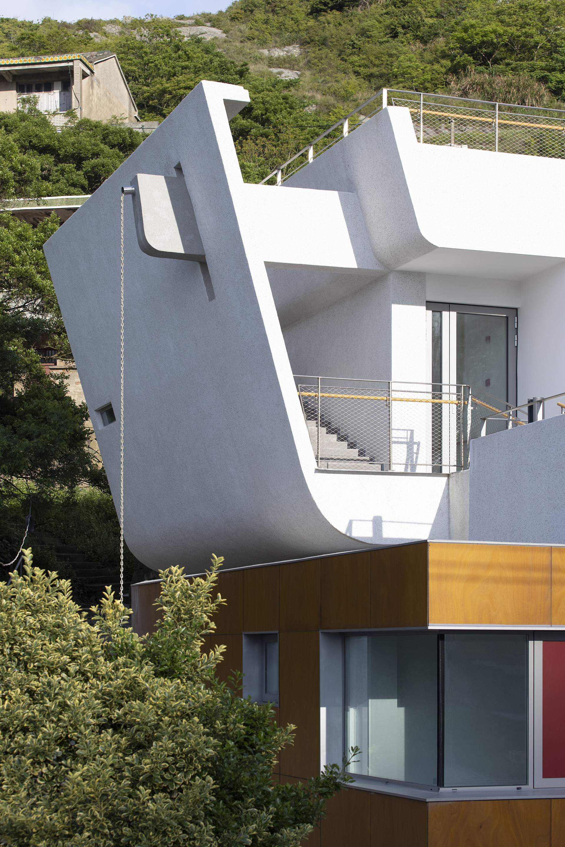 Angled white facade with metal railings and mustard-colored lower volume set against dense hillside vegetation