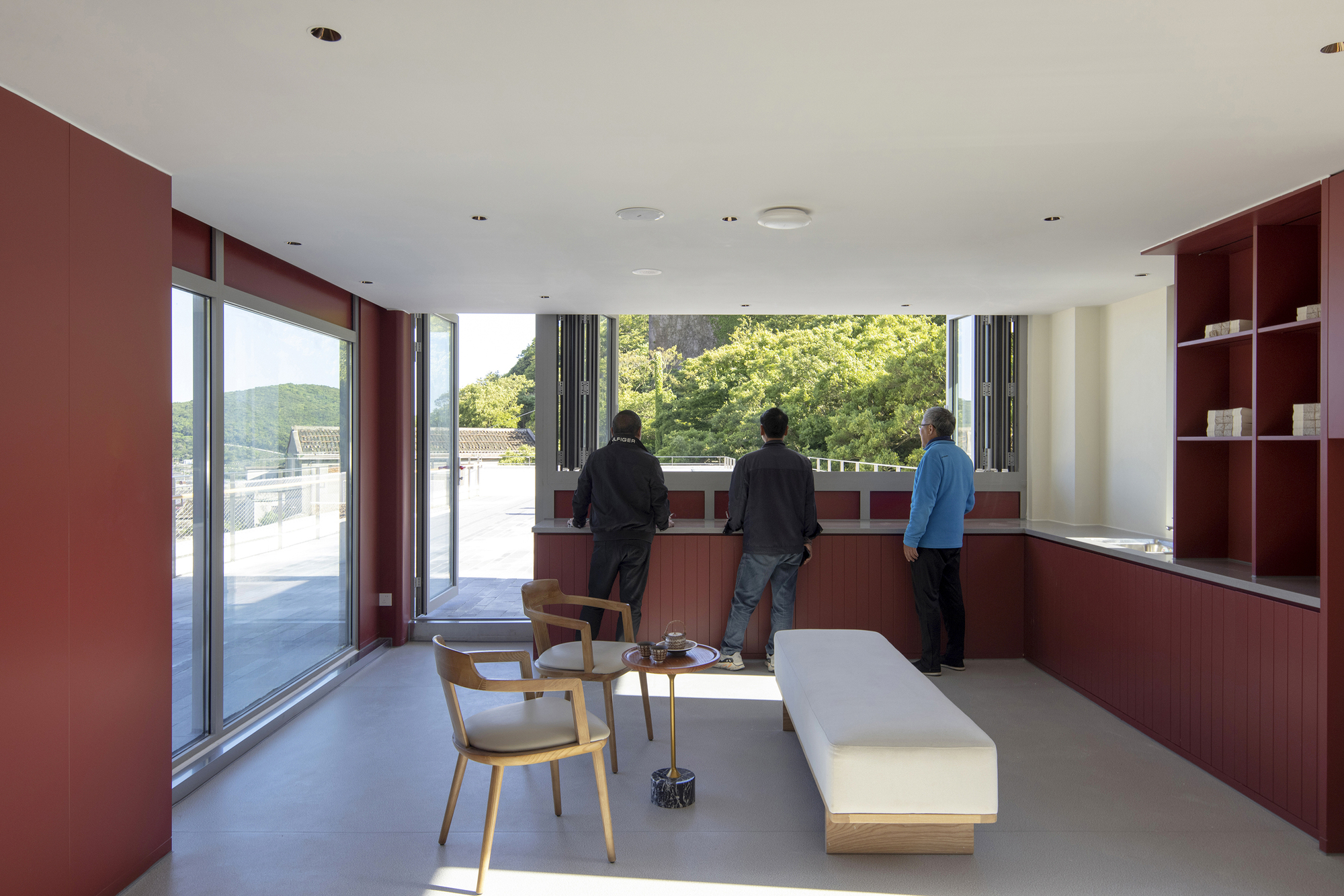 Living room with red built-in millwork and three people looking out toward treetops in daylight