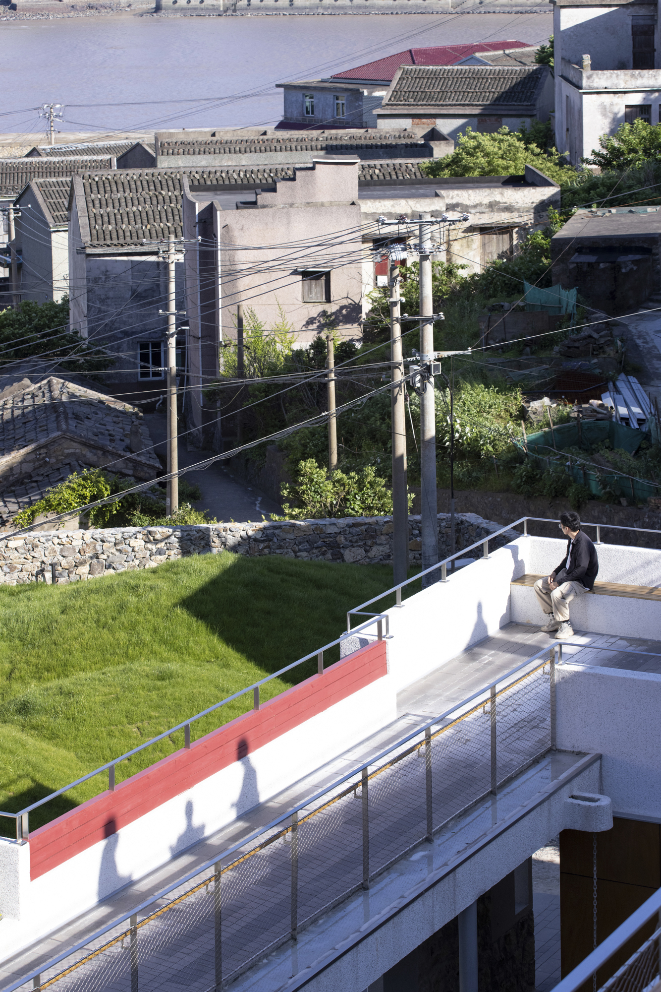 Rooftop terrace with grass lawn and metal railing overlooking neighboring rooftops and utility poles