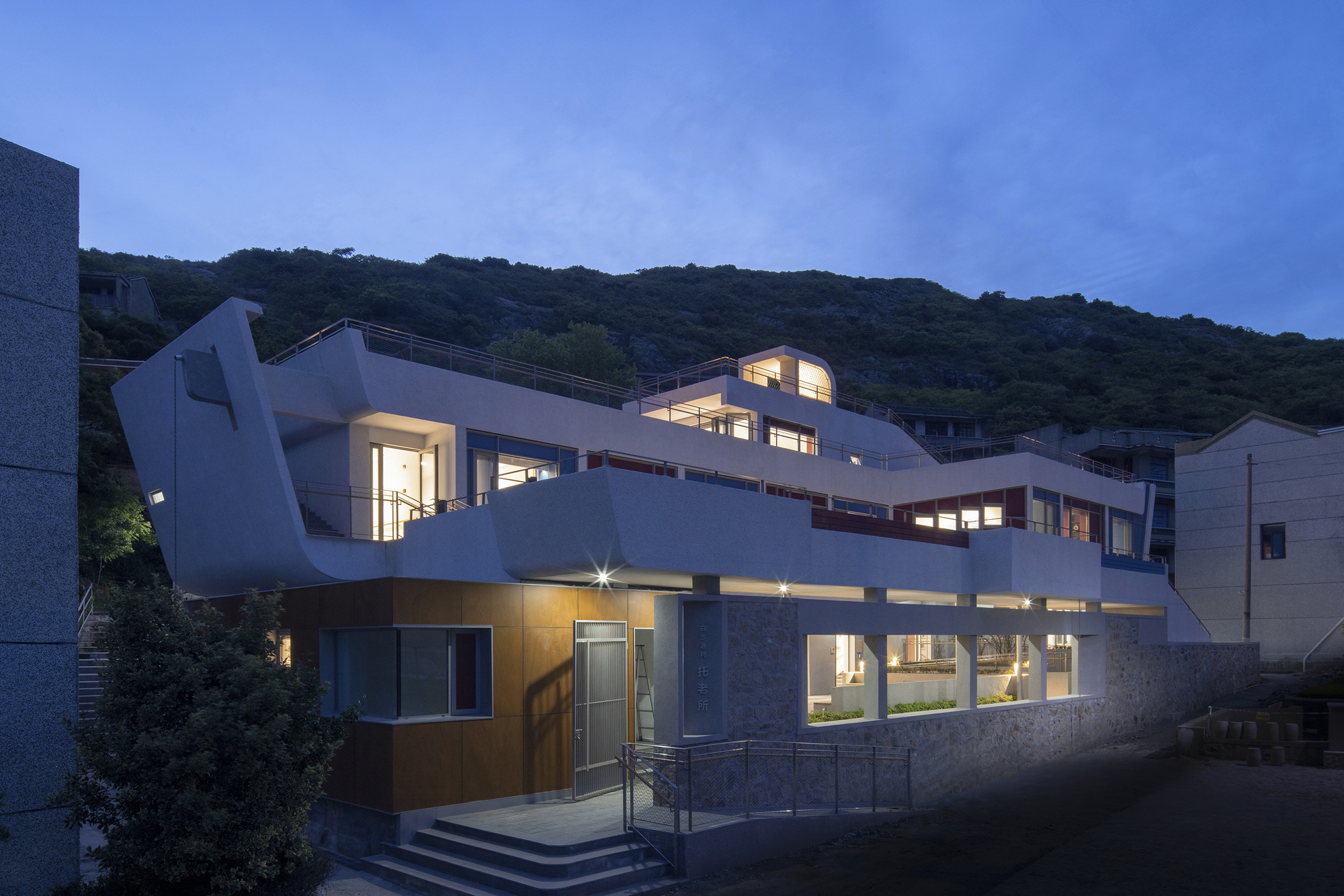Exterior view of the white terraced facade with curved roofline illuminated at dusk against a forested hillside