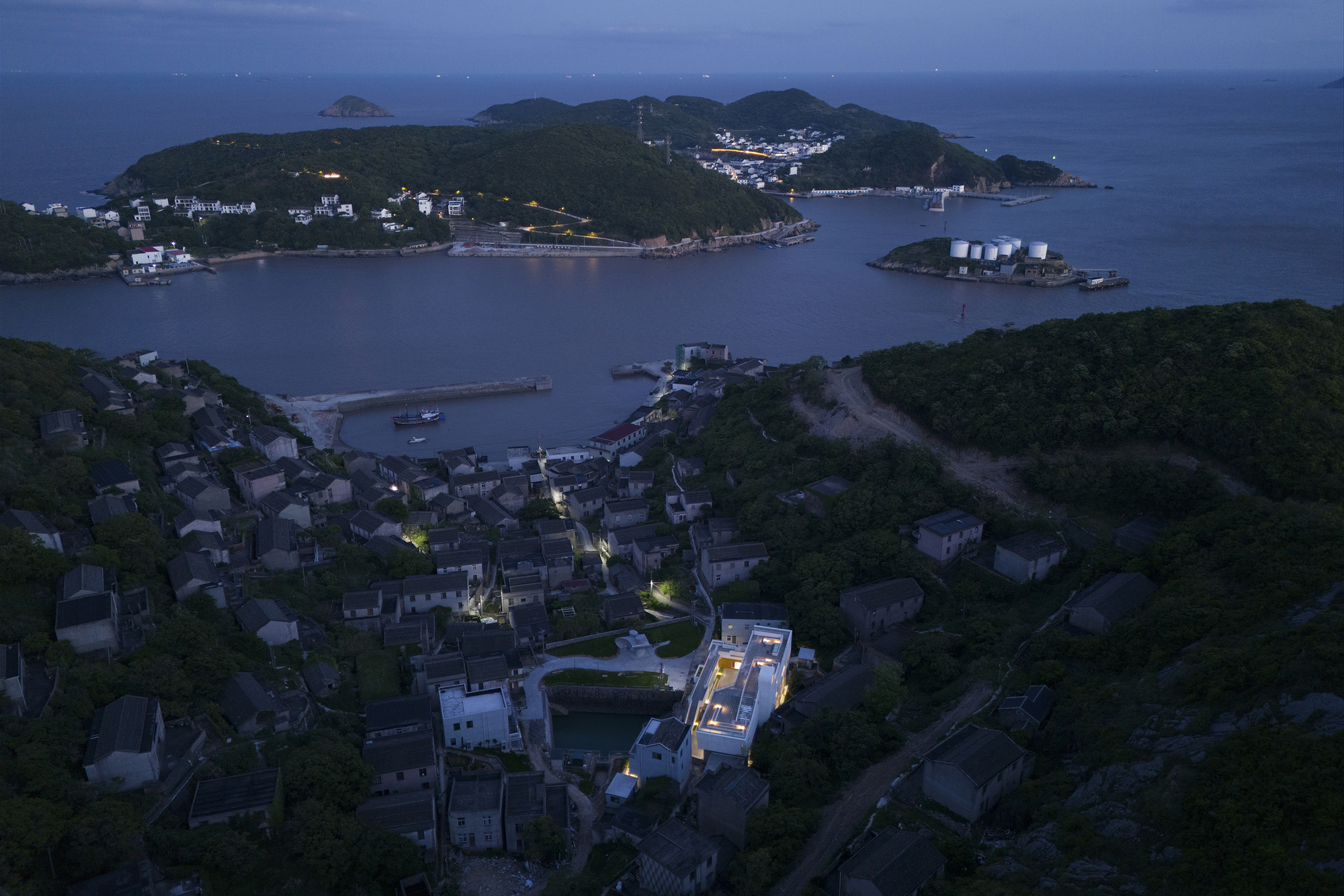 Drone view of illuminated rooftop among coastal village buildings at twilight