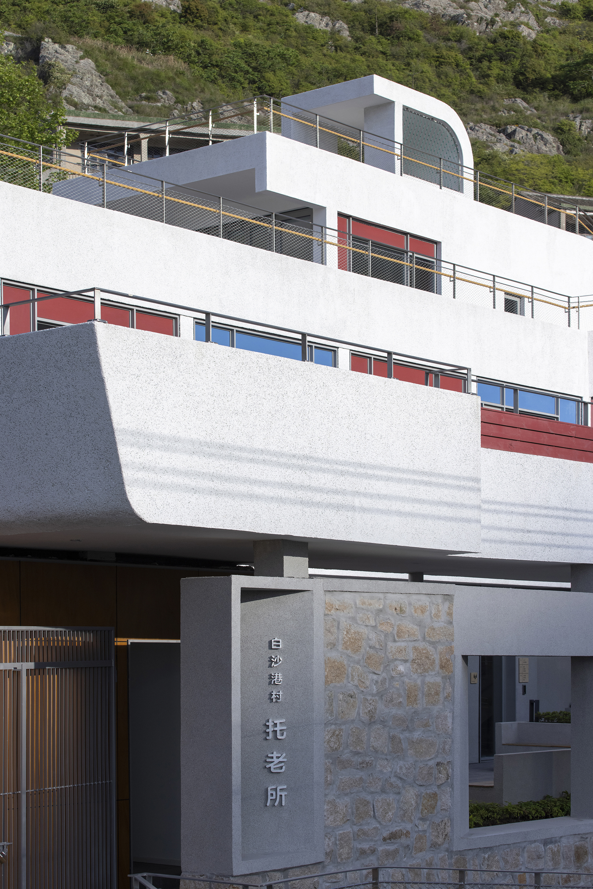 Entry gate with stone wall and signage below white terraced levels with colored window panels