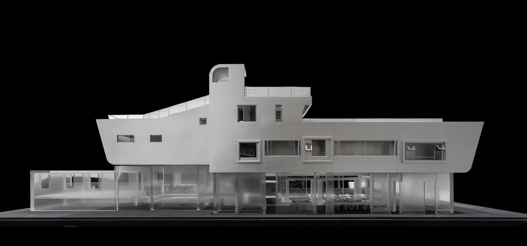 Physical model elevation showing a white two-story facade with horizontal ribbon windows and transparent ground floor