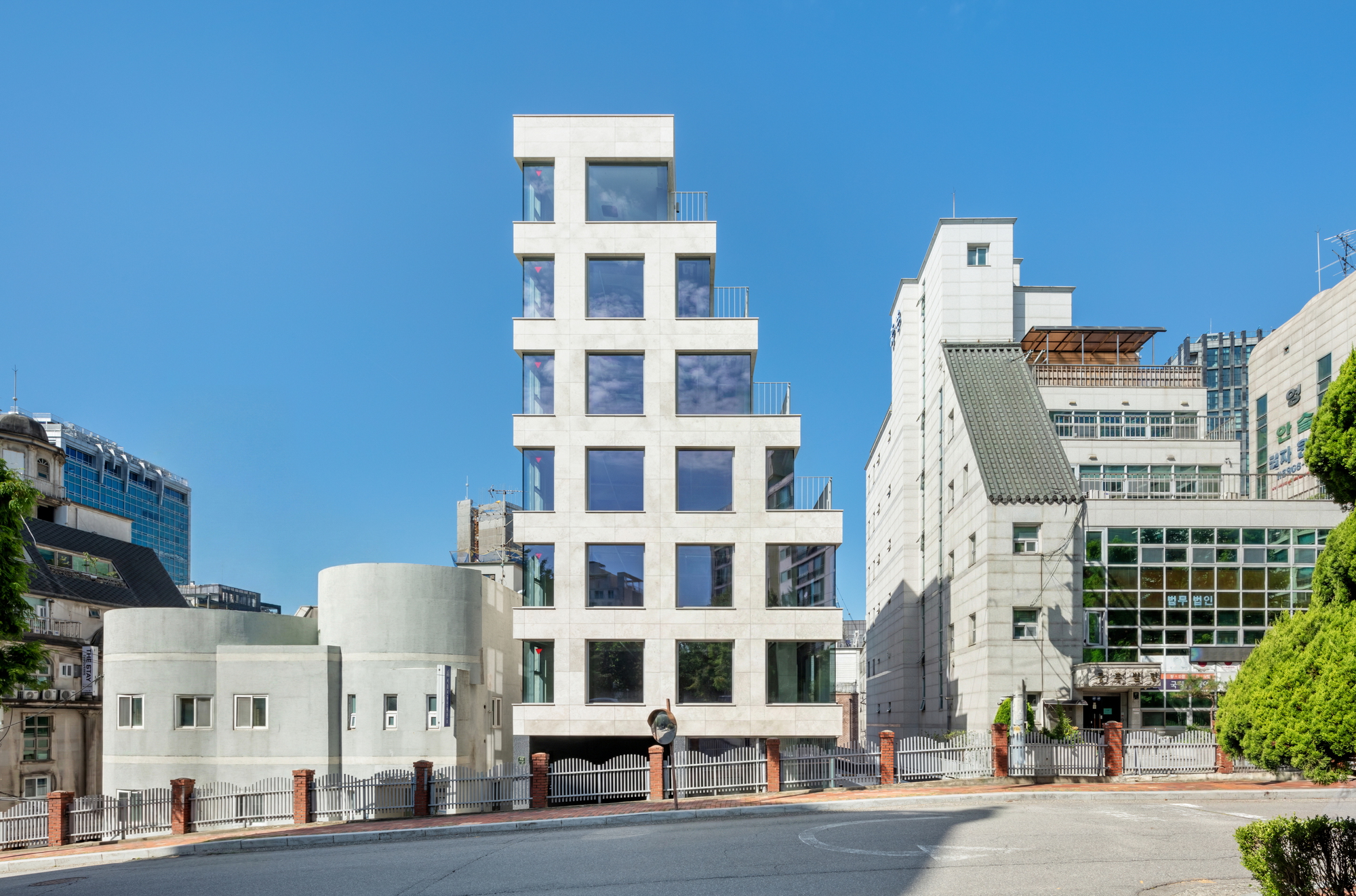 Street view of the white stepped facade rising between existing buildings on a clear day