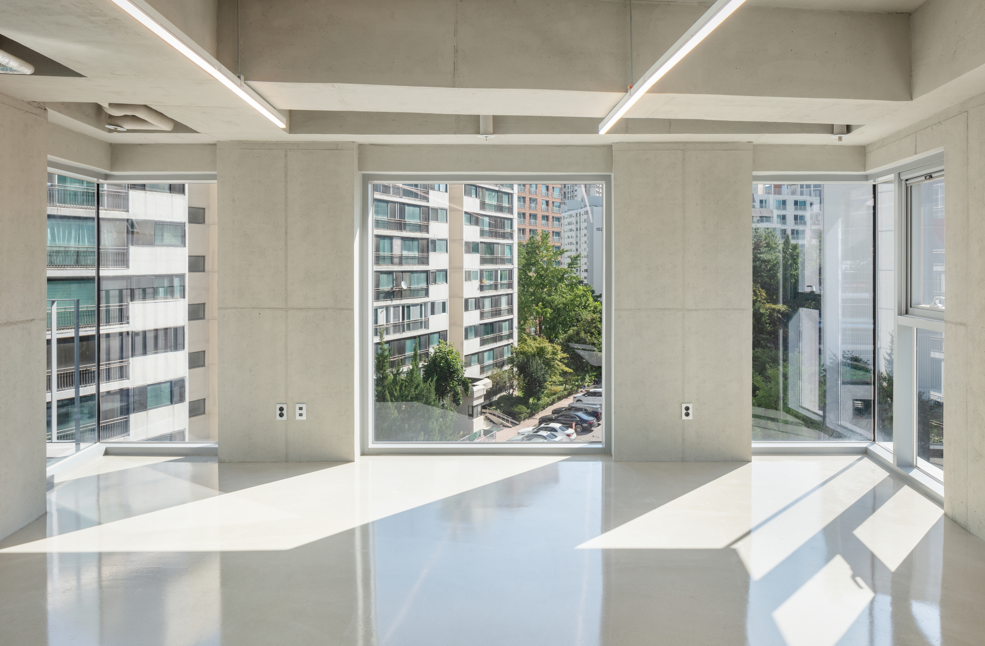 Interior space with exposed concrete ceiling beams and floor-to-ceiling windows overlooking neighboring buildings