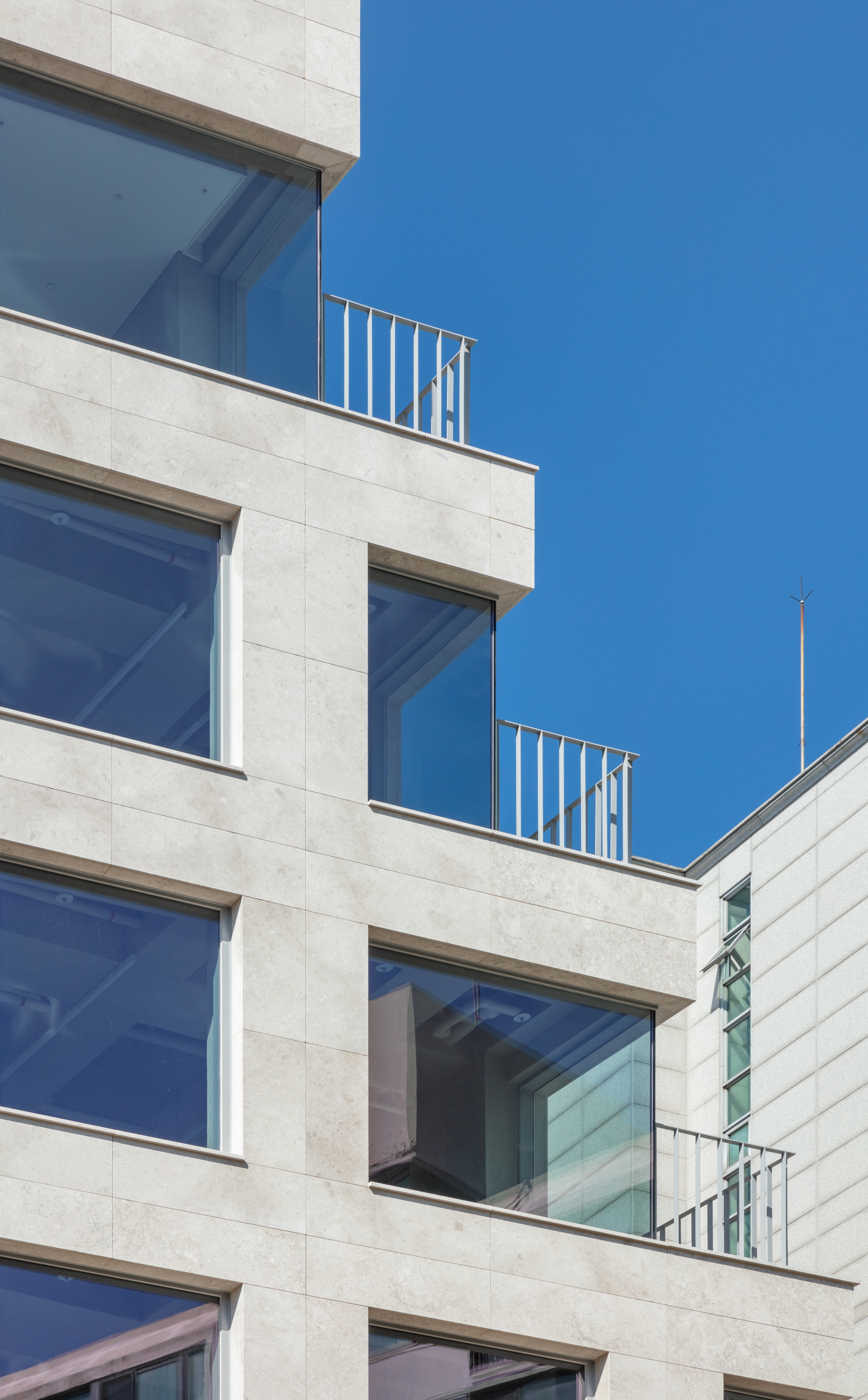 Stepped balconies with metal railings set into the stone facade under clear blue sky
