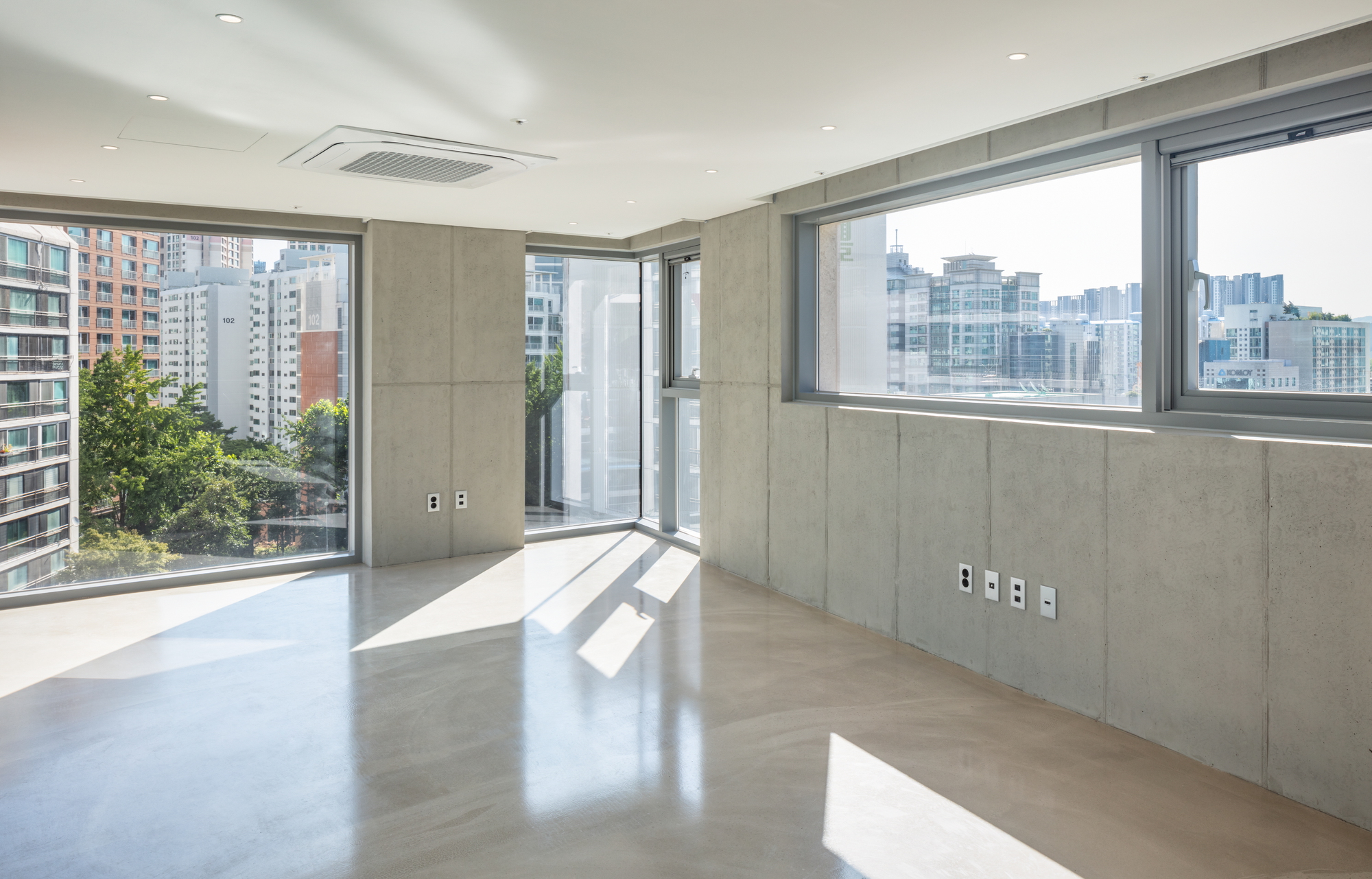 Corner interior with concrete panel walls and floor-to-ceiling windows overlooking the dense urban skyline