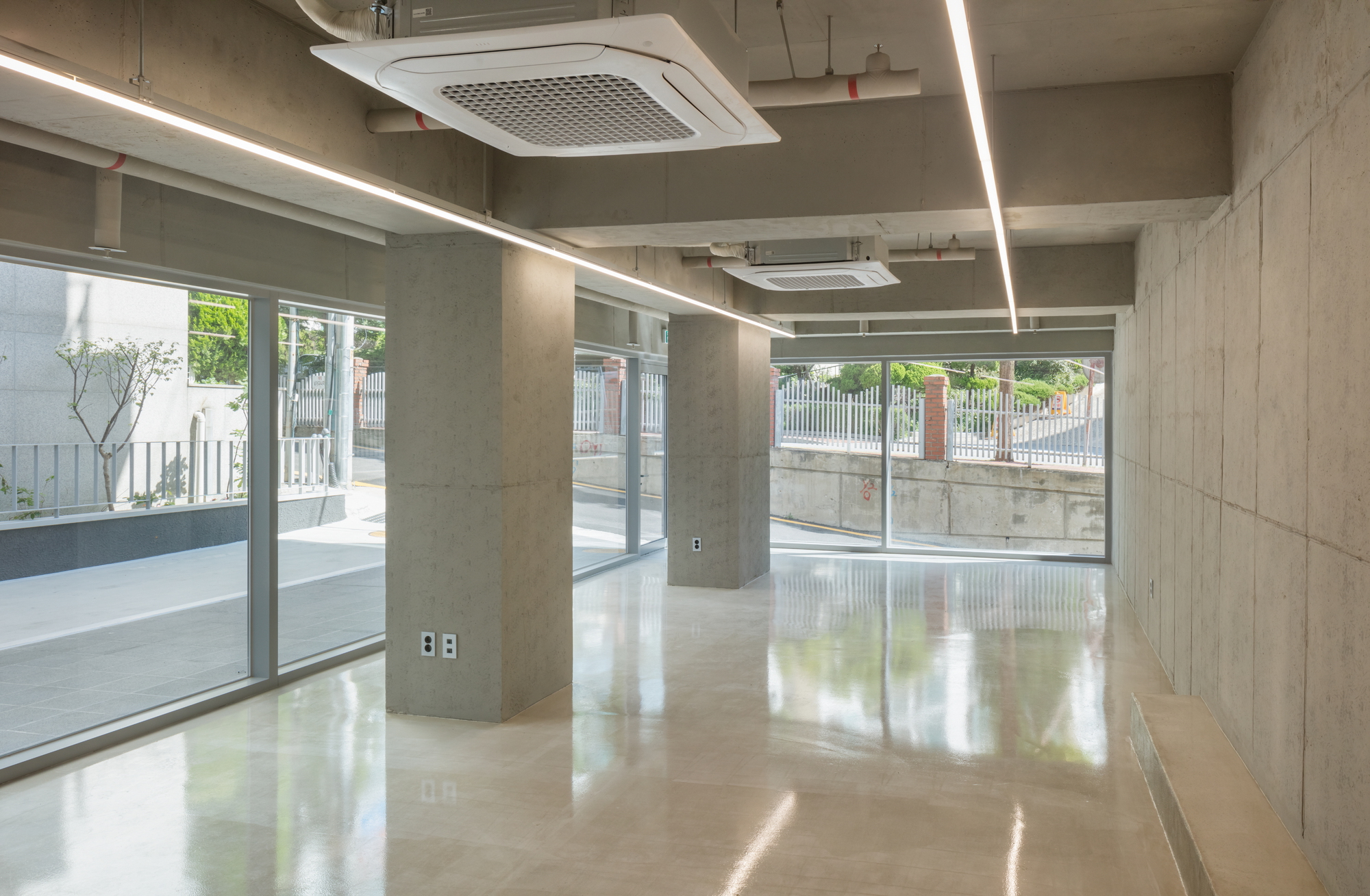 Open floor space with exposed concrete columns, linear light fixtures, and glazed storefronts along the street