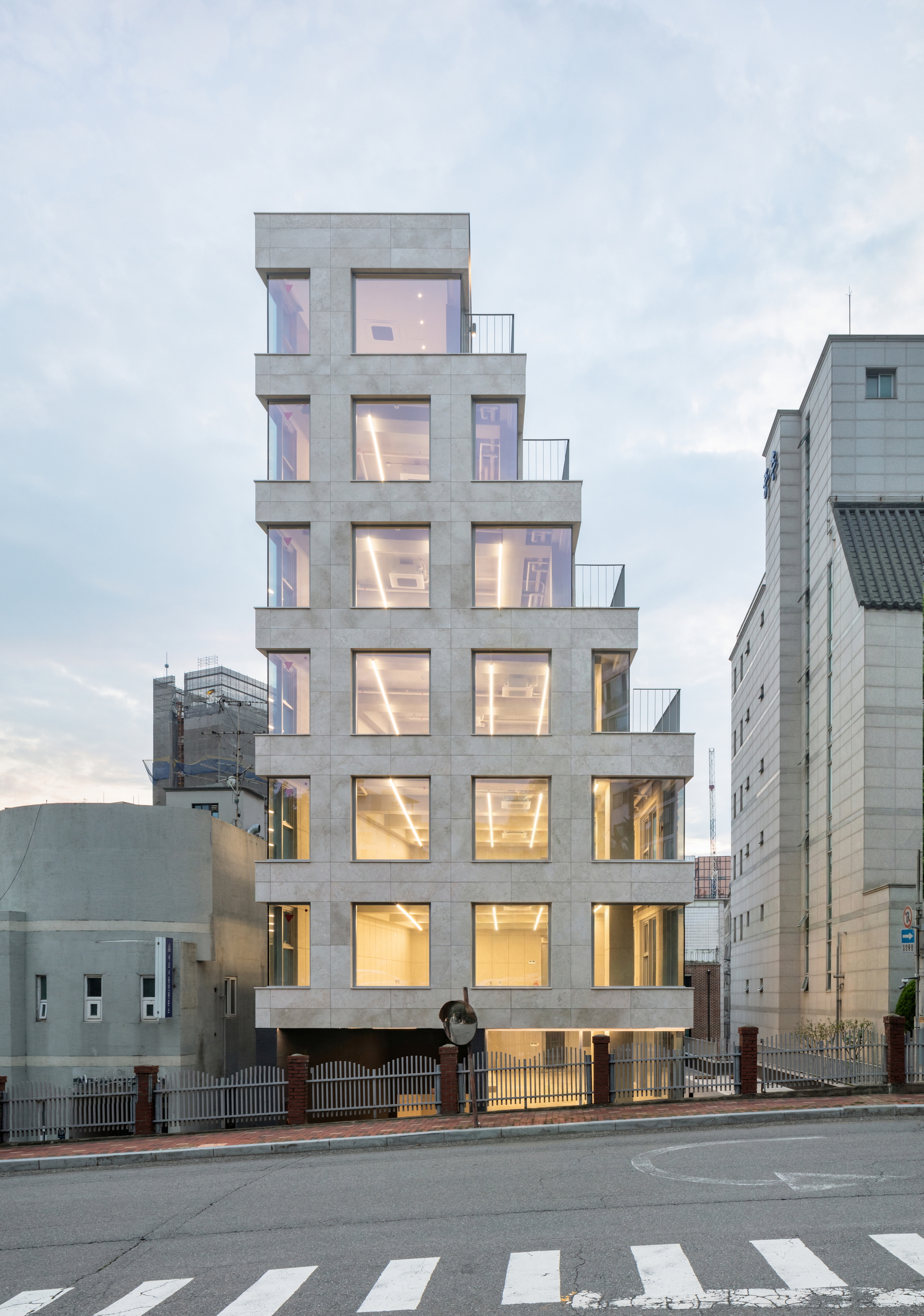 Street view of the stepped concrete facade with illuminated interiors at dusk