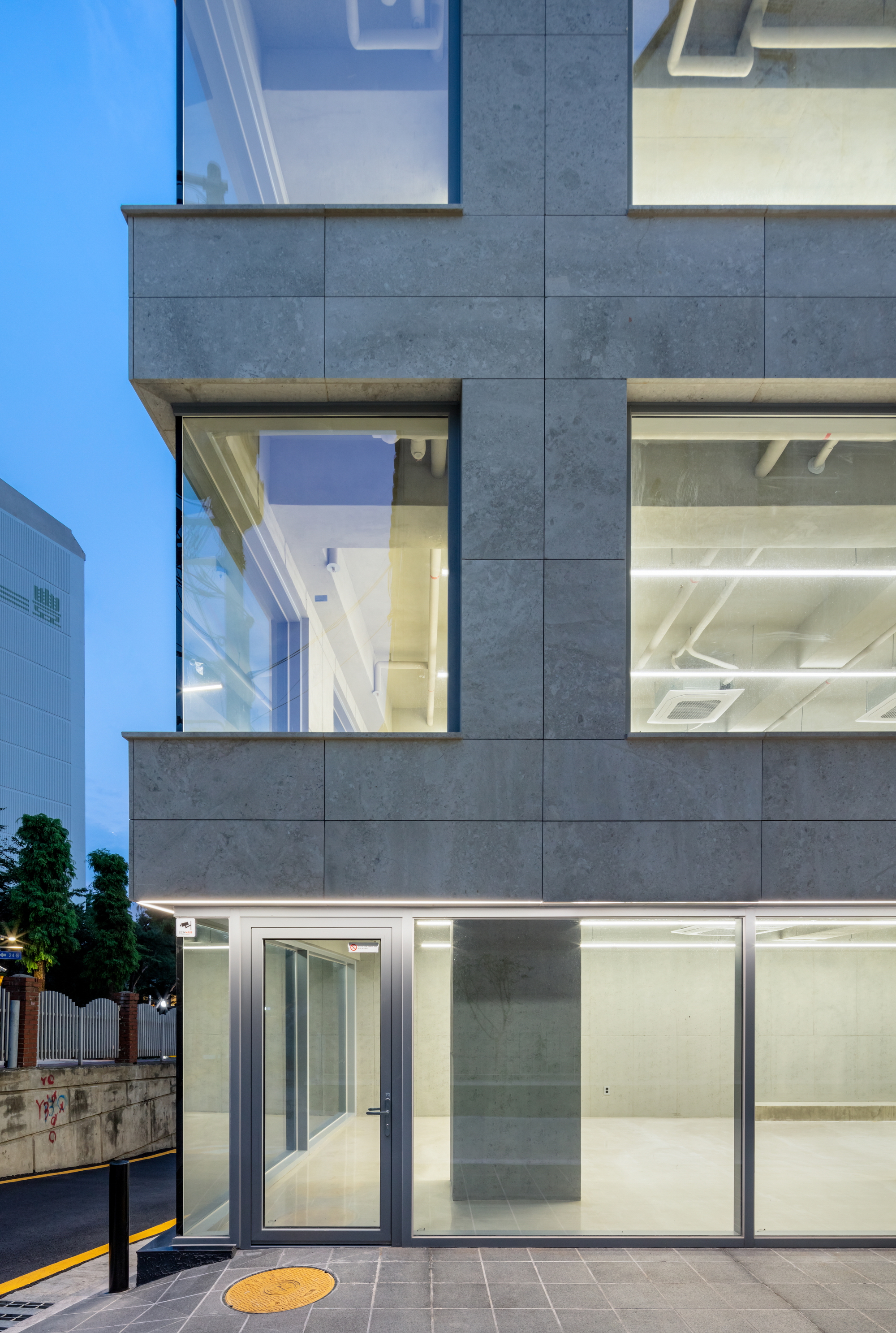 Corner view of the grey panel facade with floor-to-ceiling glazing illuminated at dusk