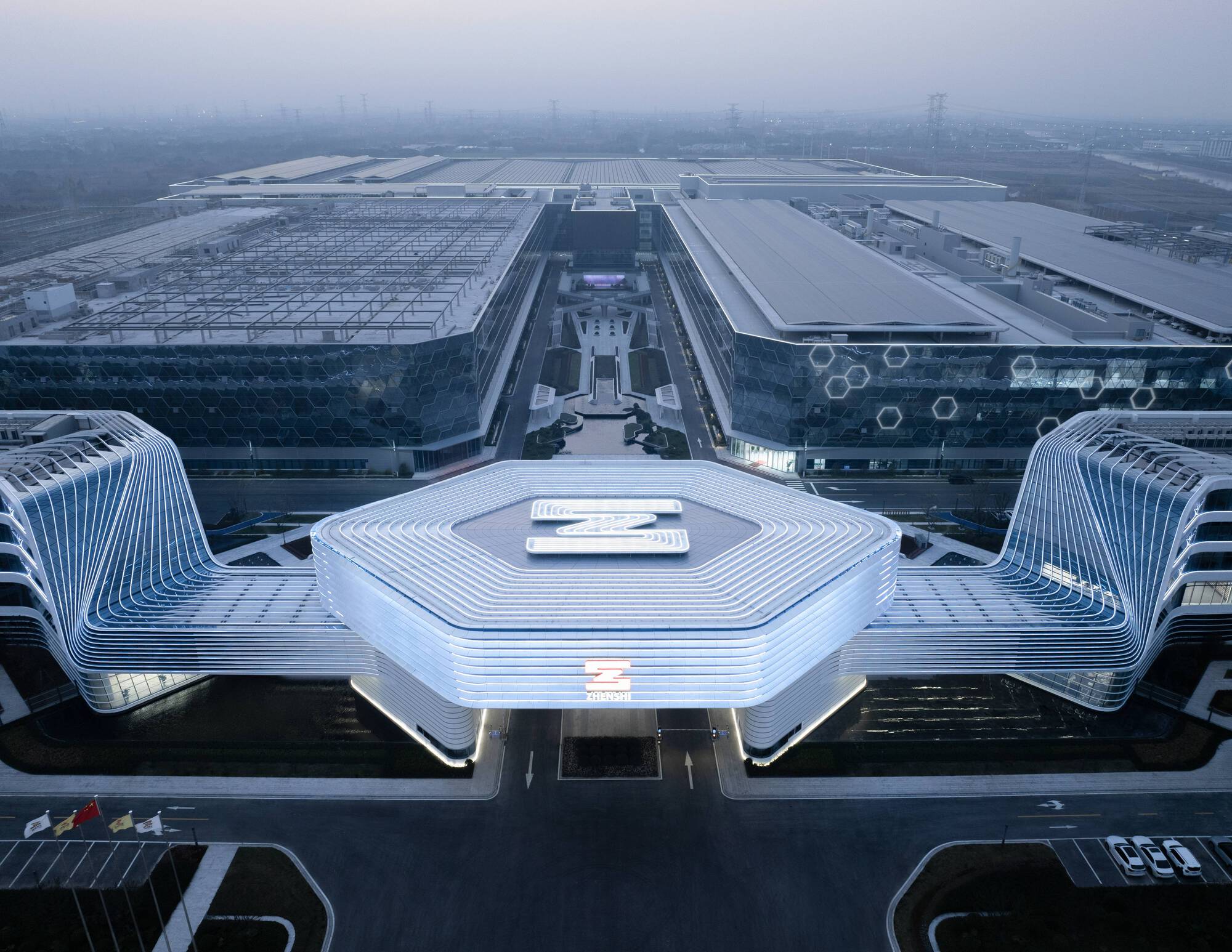 Aerial view of the hexagonal central canopy flanked by curved ribbed pavilions and linear exhibition halls in hazy daylight