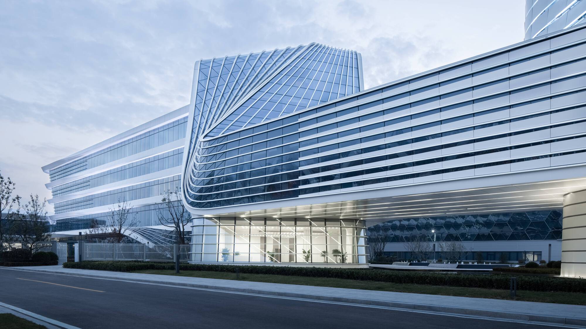 Street view of the horizontal banded facade wrapping a curved corner with a glass-enclosed ground floor at dusk