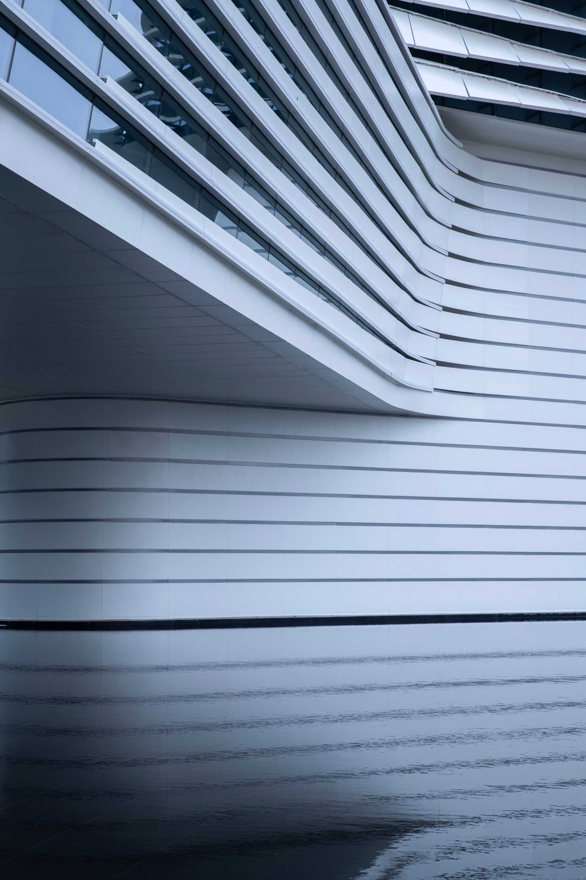 Close-up of the horizontal metal fins curving across the facade with wet pavement reflecting below