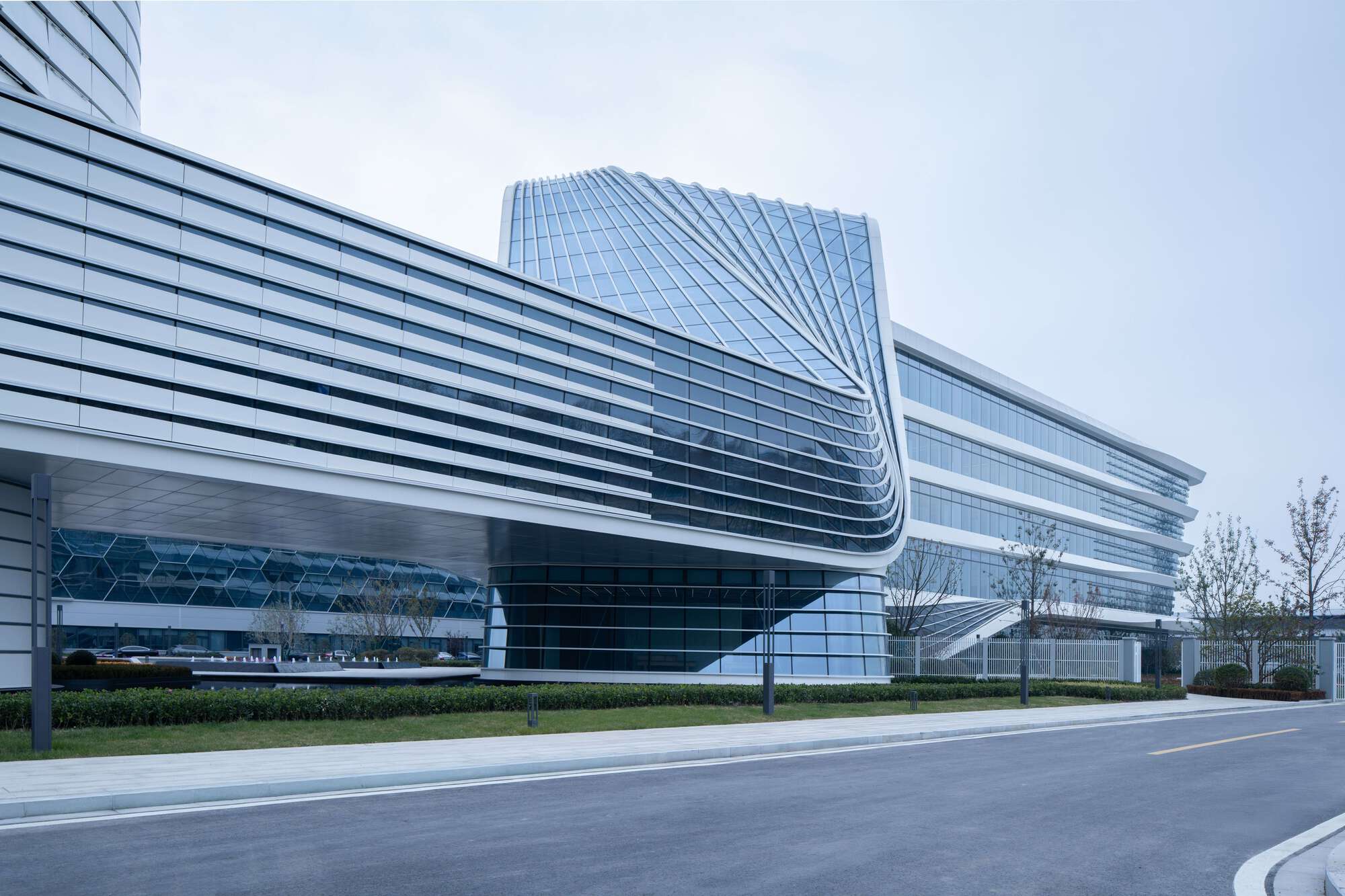 Street view of the layered horizontal facade with hexagonal glass building behind bare trees