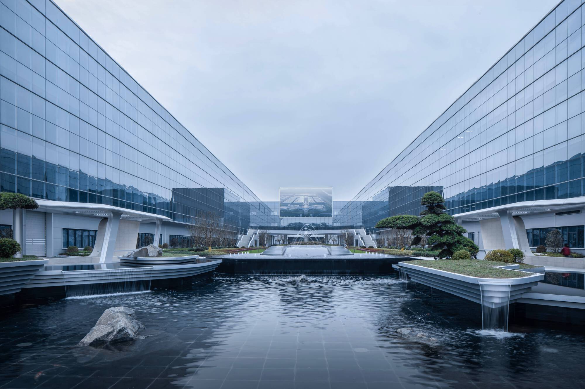 Central water feature with planted terraces framed by symmetrical glass facades at dusk