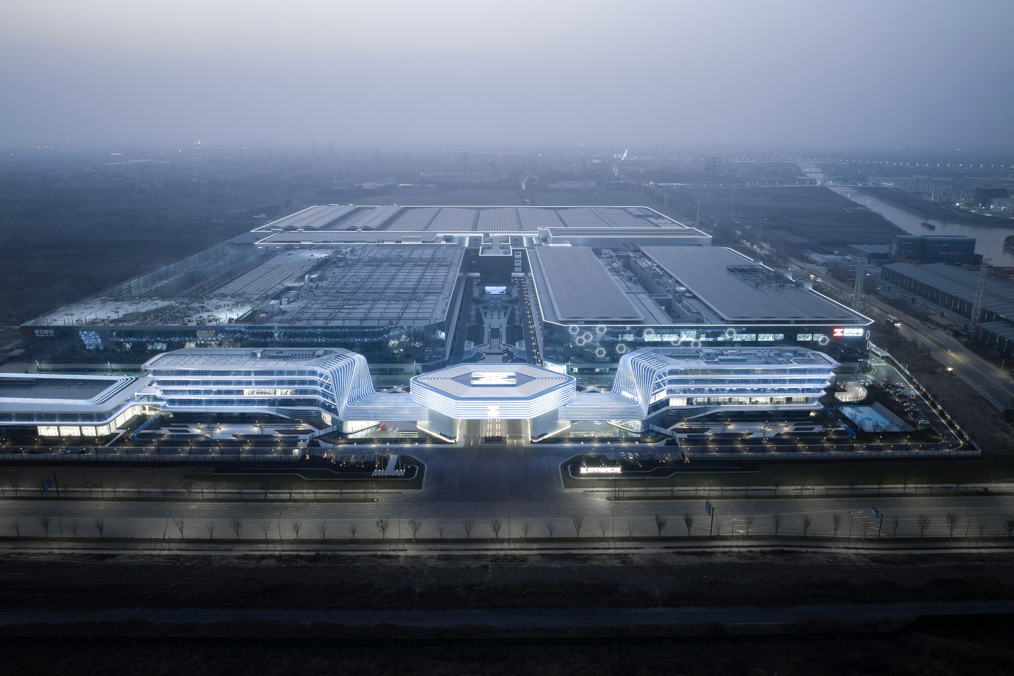 Aerial view of the illuminated white complex with curved wings and central pavilion at dusk