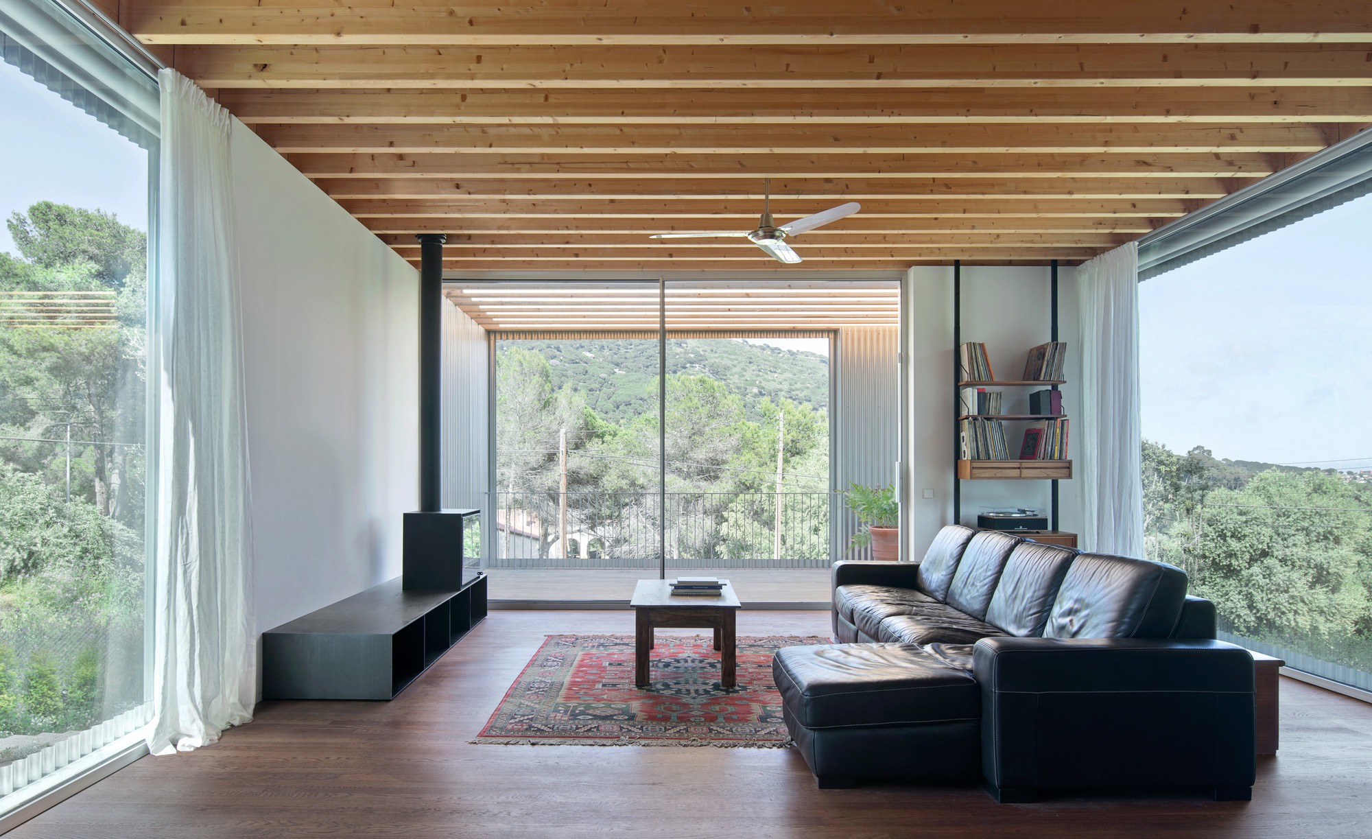 Living room with exposed timber ceiling joists and floor-to-ceiling glazing overlooking wooded hillside