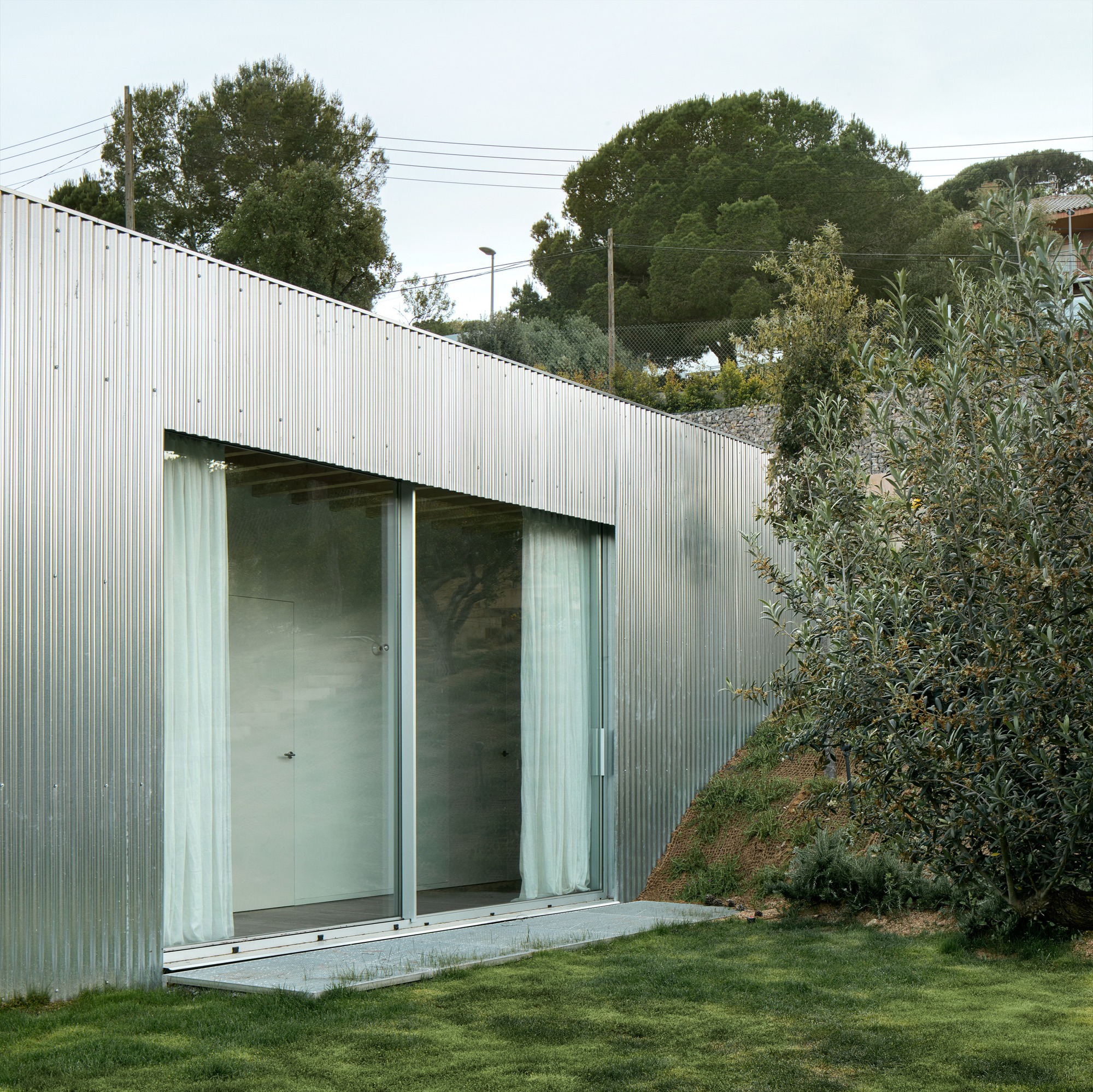 Ground floor volume clad in corrugated metal with sliding glass doors opening to lawn