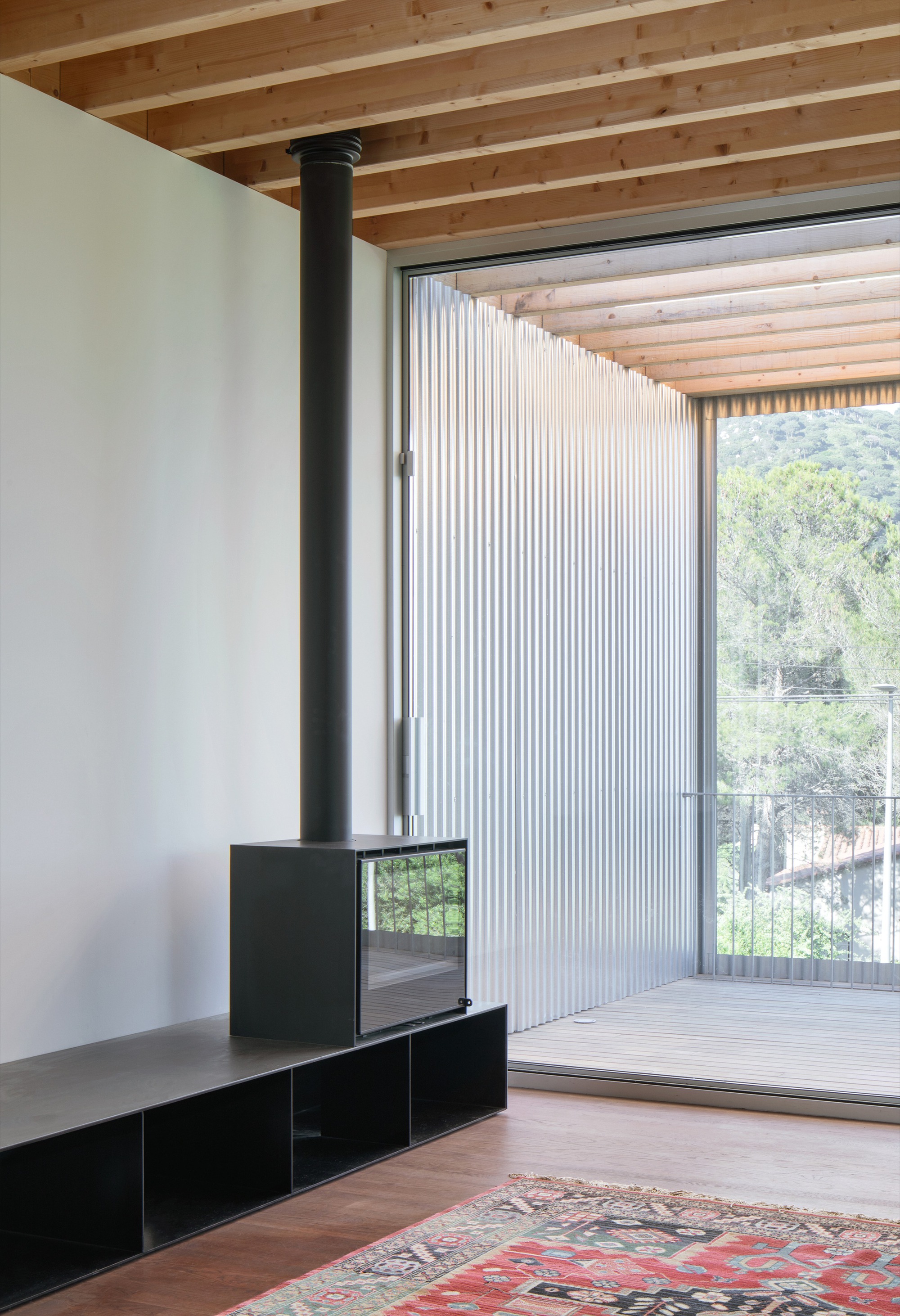 Interior room with black steel wood stove and exposed timber beam ceiling looking out to deck with vertical metal cladding